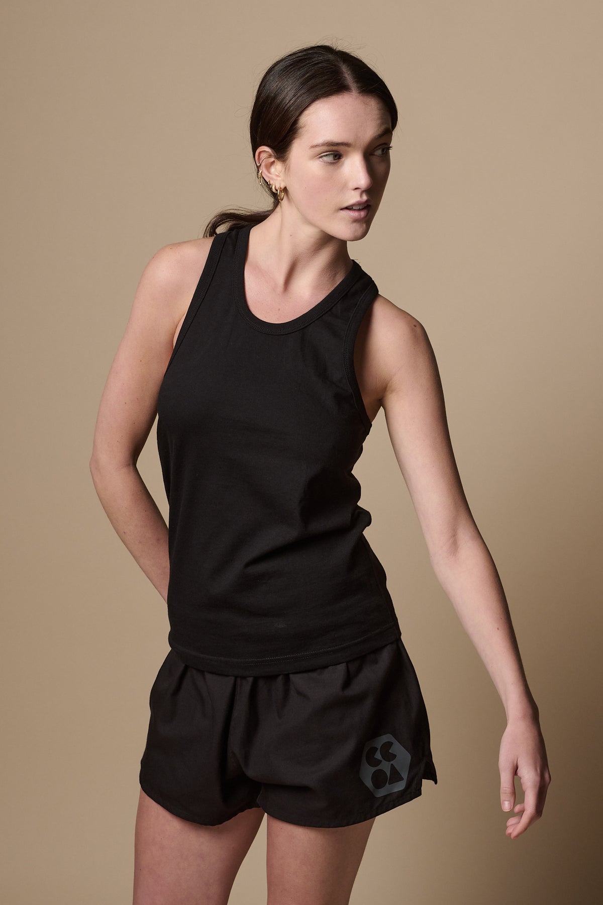 Image shows white female with brunette hair in ponytail, wearing racer back vest plastic free in black