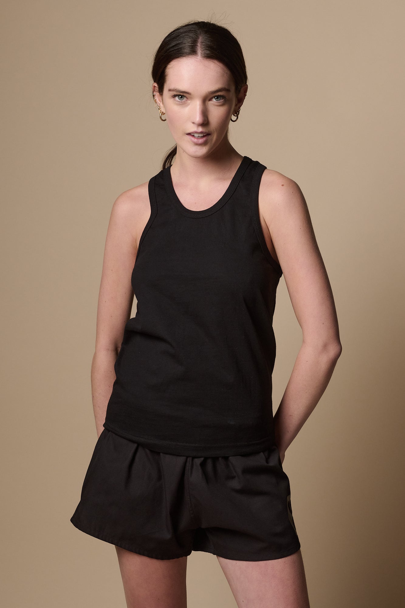 Image shows thigh up of female wearing racer back vest in black