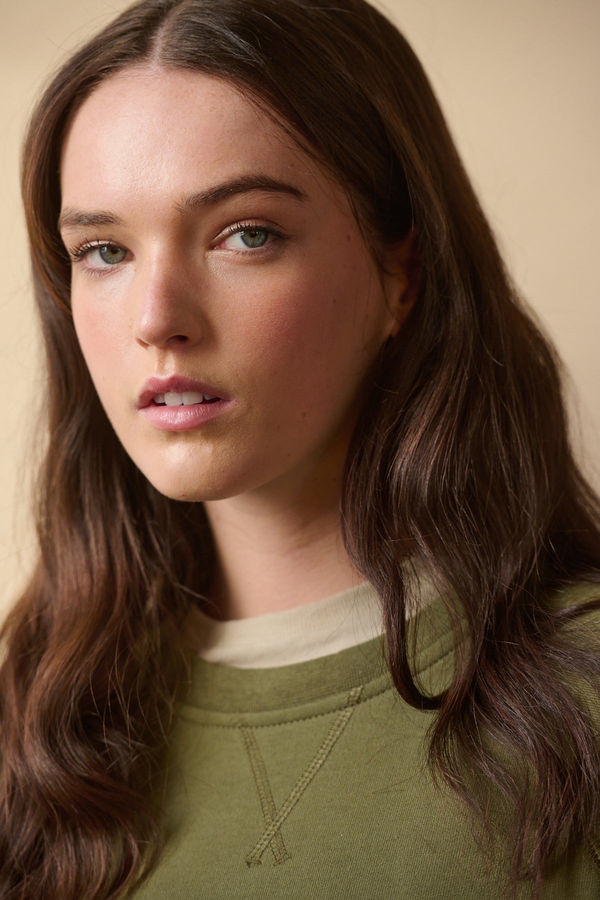 Portrait of brunette female wearing raglan sweatshirt in olive layered over t shirt in stone