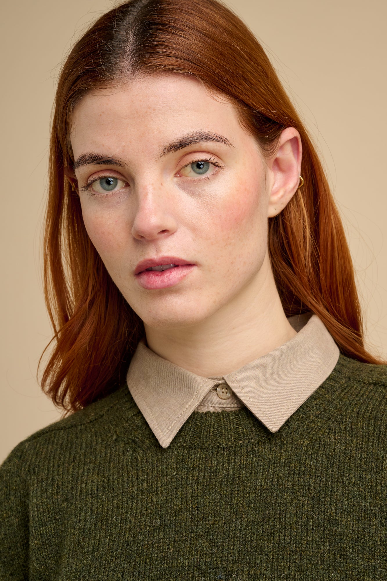 Woman wearing a green sweater with a beige shirt collar against a beige background.