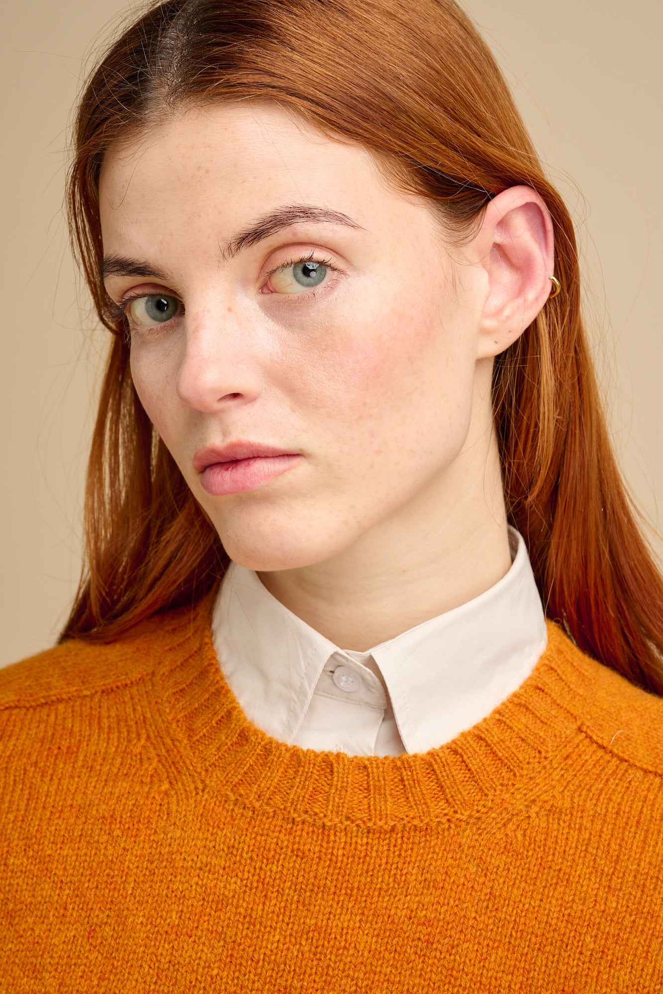 Person wearing an orange sweater over a white shirt against a beige background
