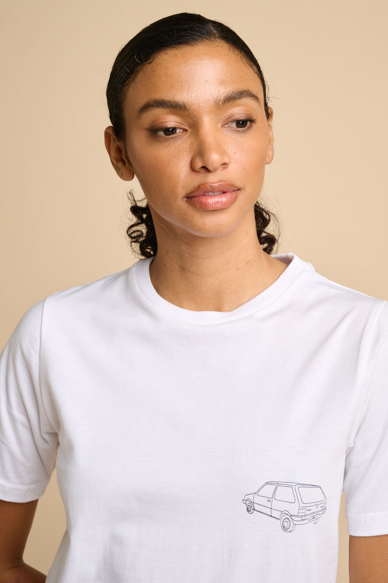 Woman wearing a white t-shirt with a small graphic on a beige background
