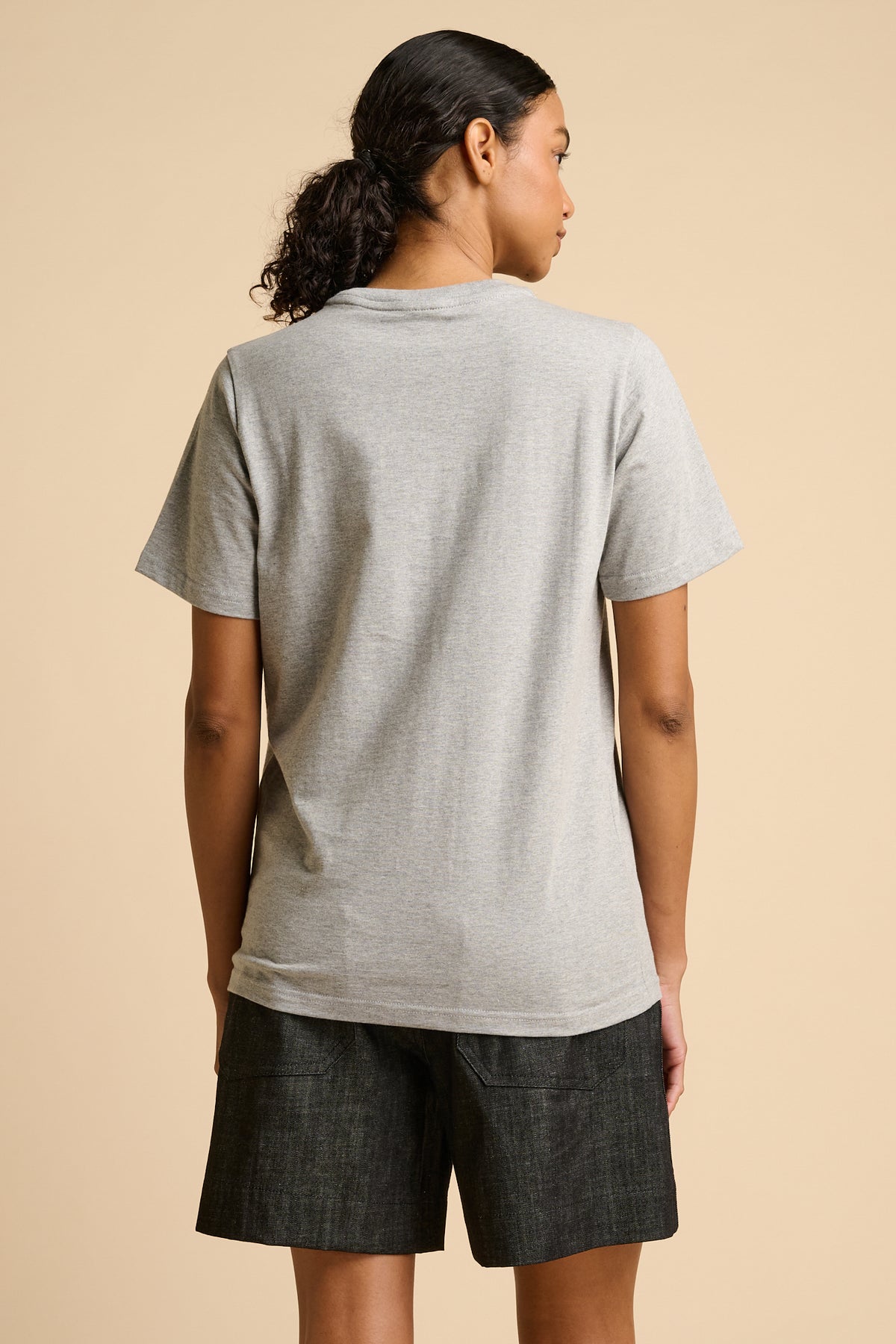 Woman wearing a grey t-shirt and dark shorts on a beige background.
