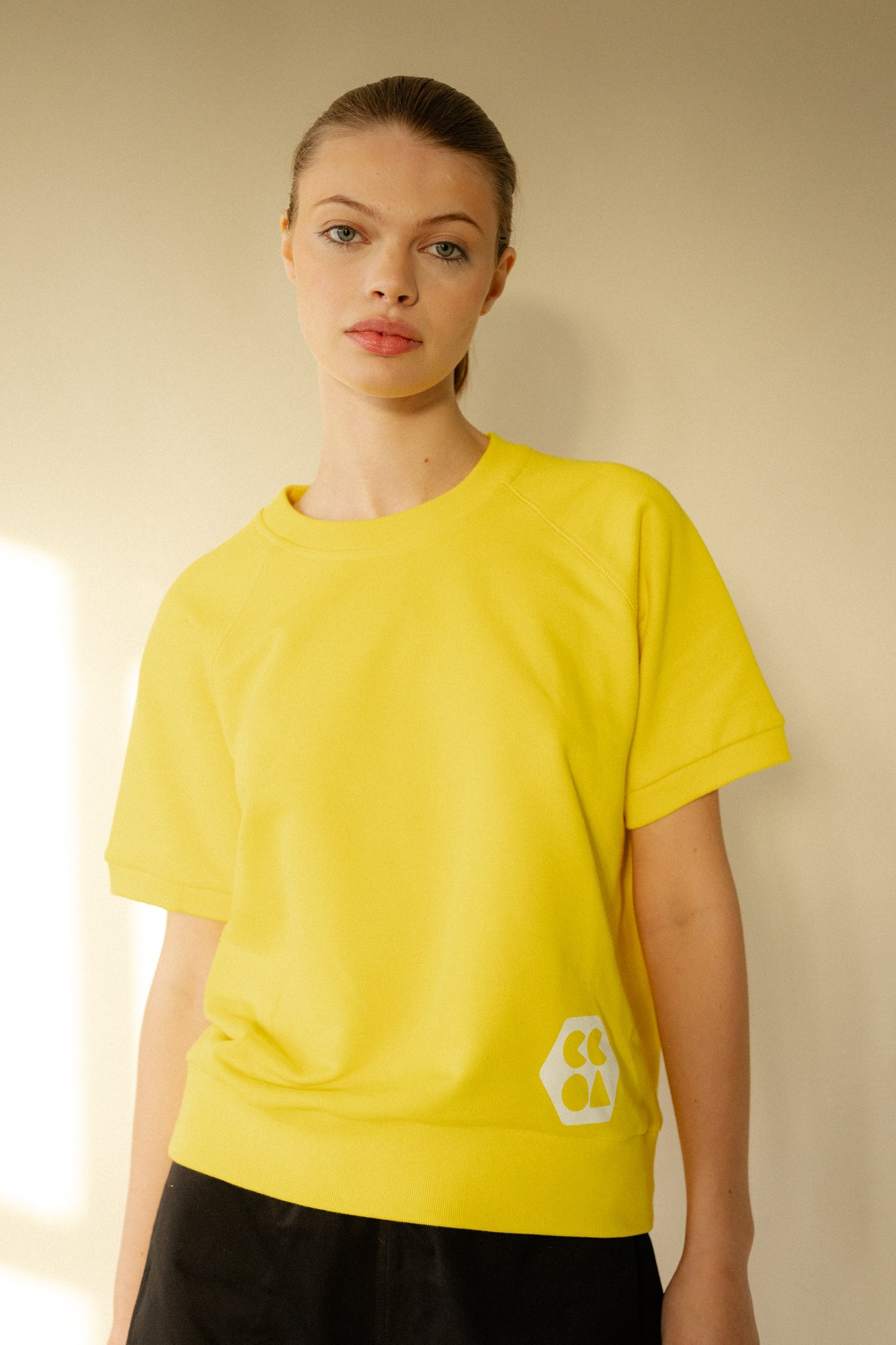 Smiley, white female wearing short sleeve raglan training top in Canary Yellow with white CCOA Logo.