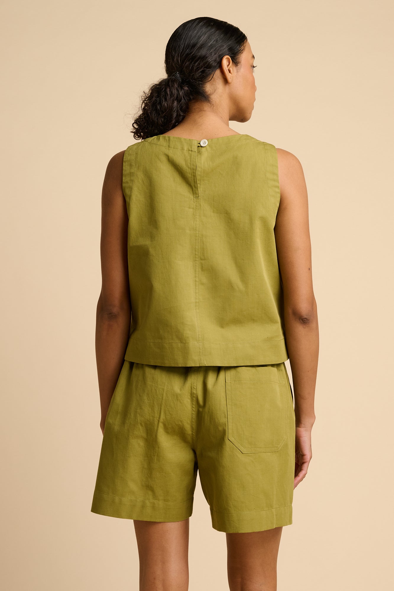 Woman wearing a green sleeveless top and shorts against a beige background.