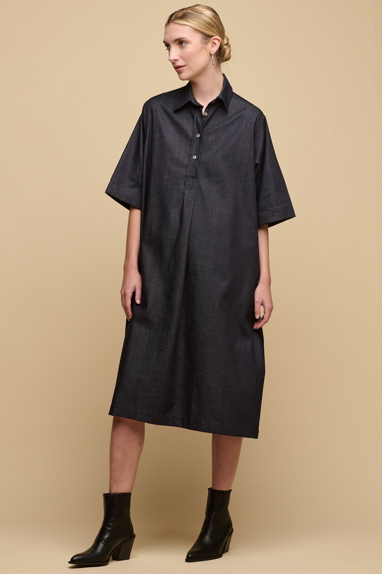 Full body image of female wearing straight denim dress in indigo without belt tie for looser fit.