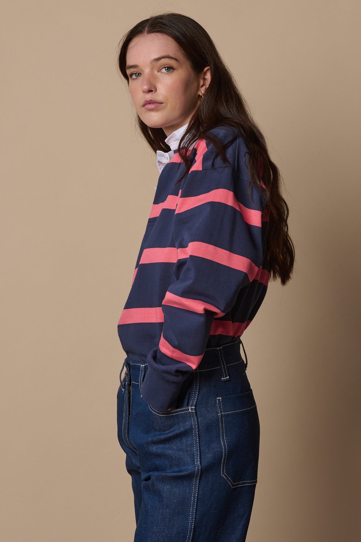 Image of the side of female wearing stripe rugby shirt in navy from the side with hand in jean pocket