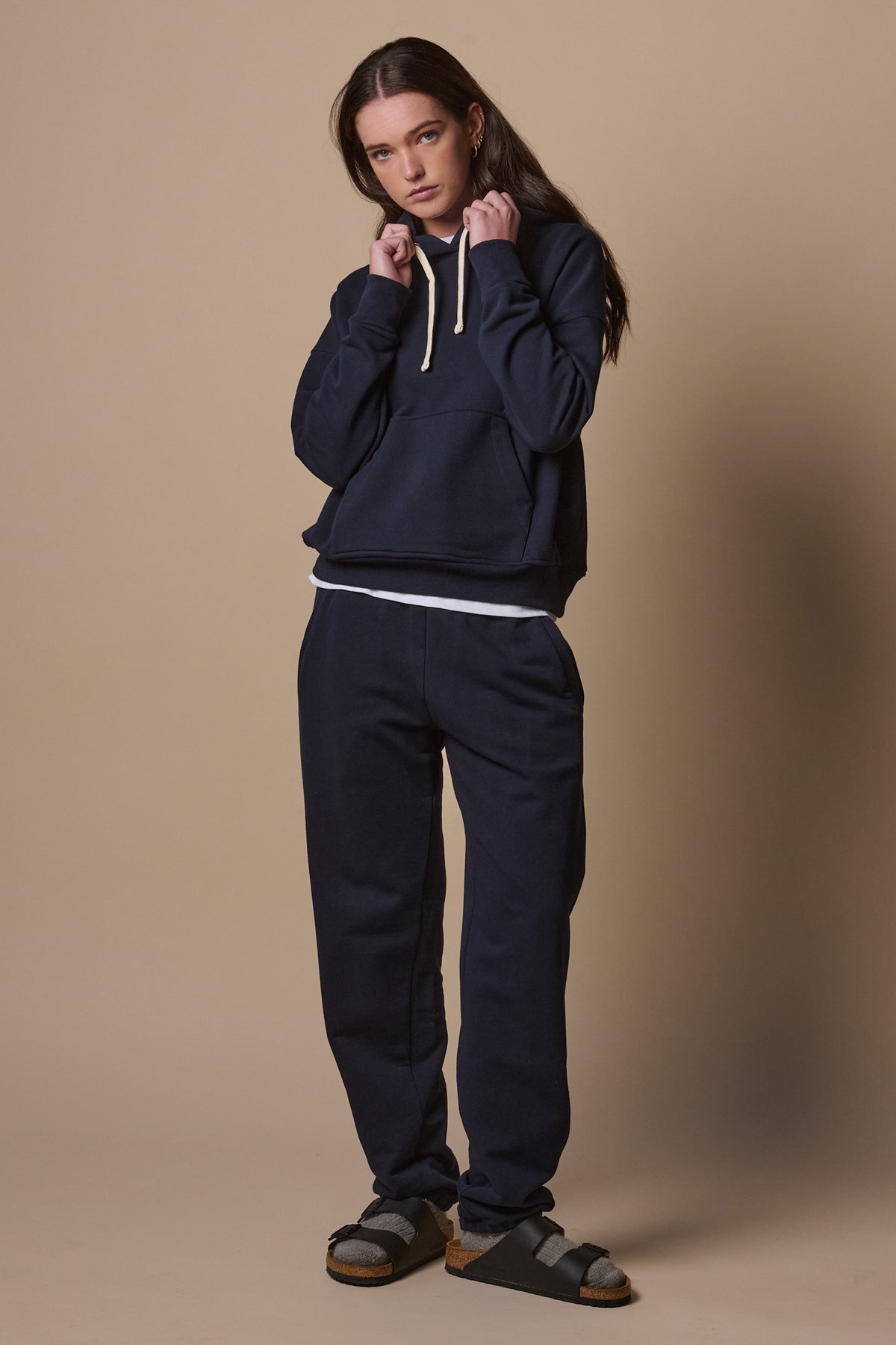 Full body image of female wearing sweatpants in navy paired with matching hooded sweatshirt 