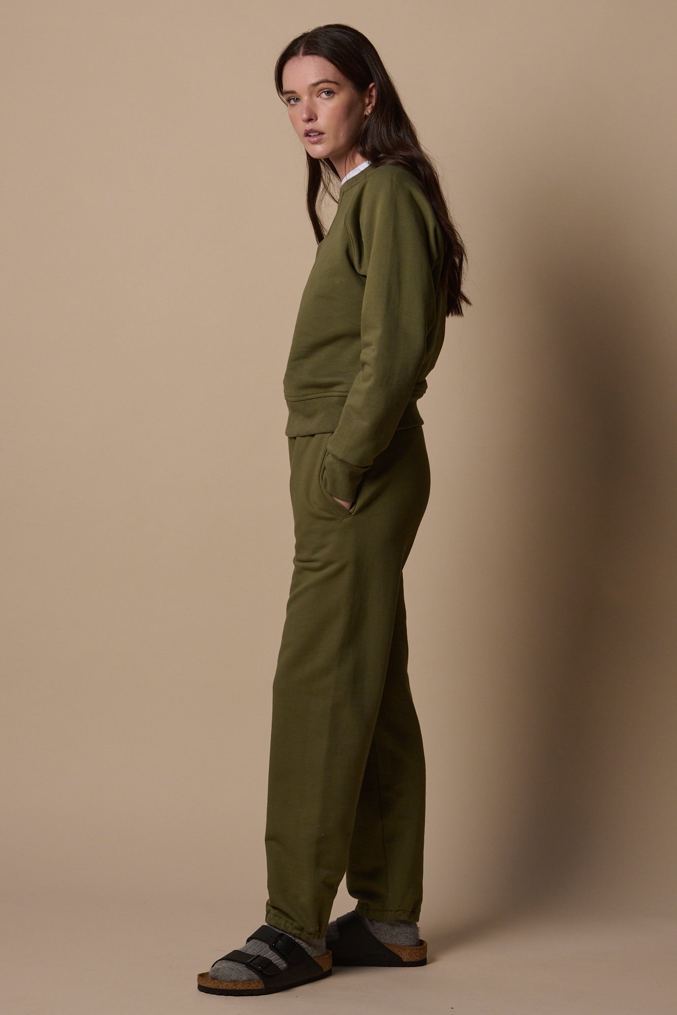 Full body side view of white female wearing sweatpants in olive with matching olive sweatshirt 