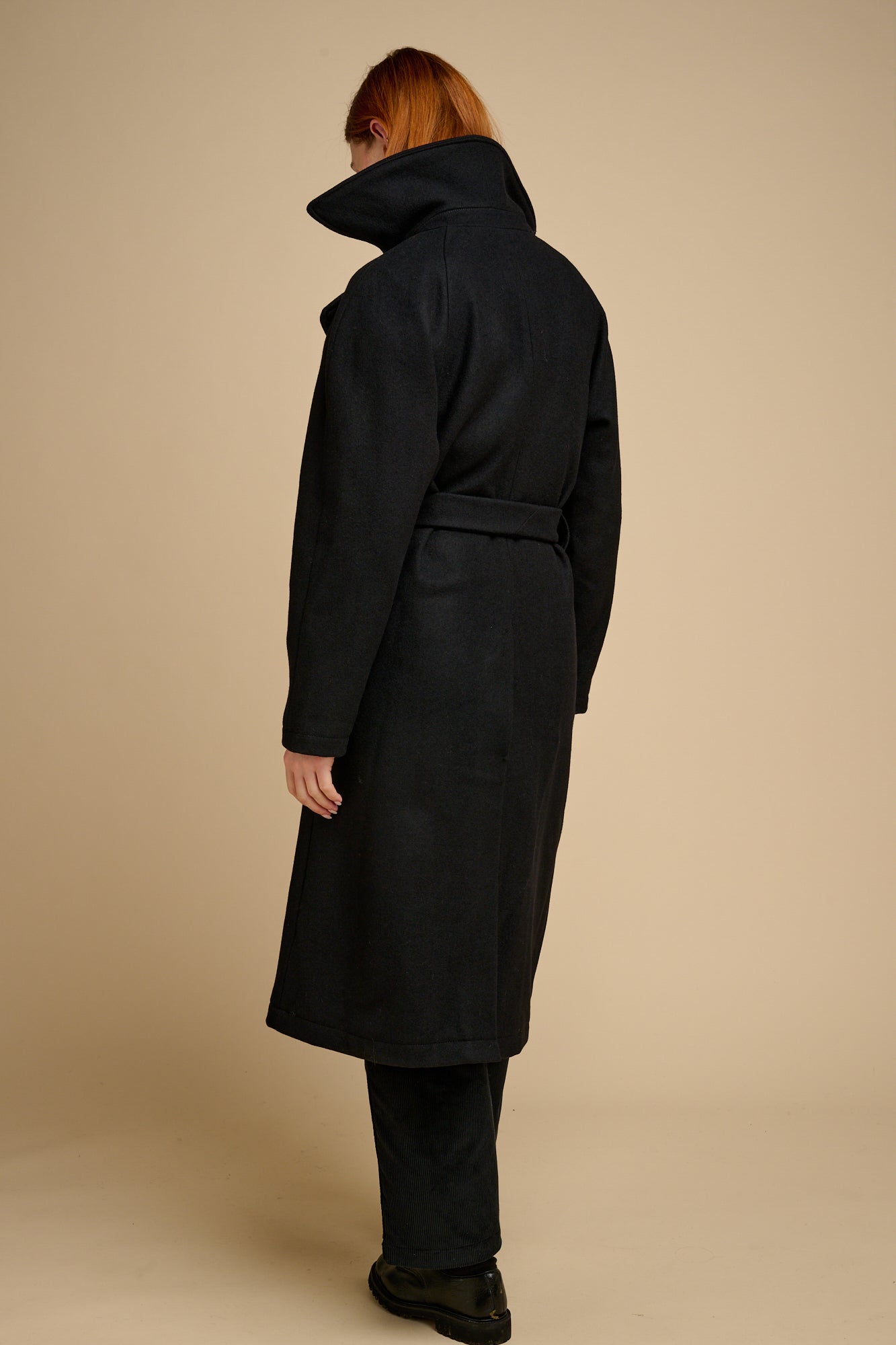 Person wearing a black coat against a beige background.