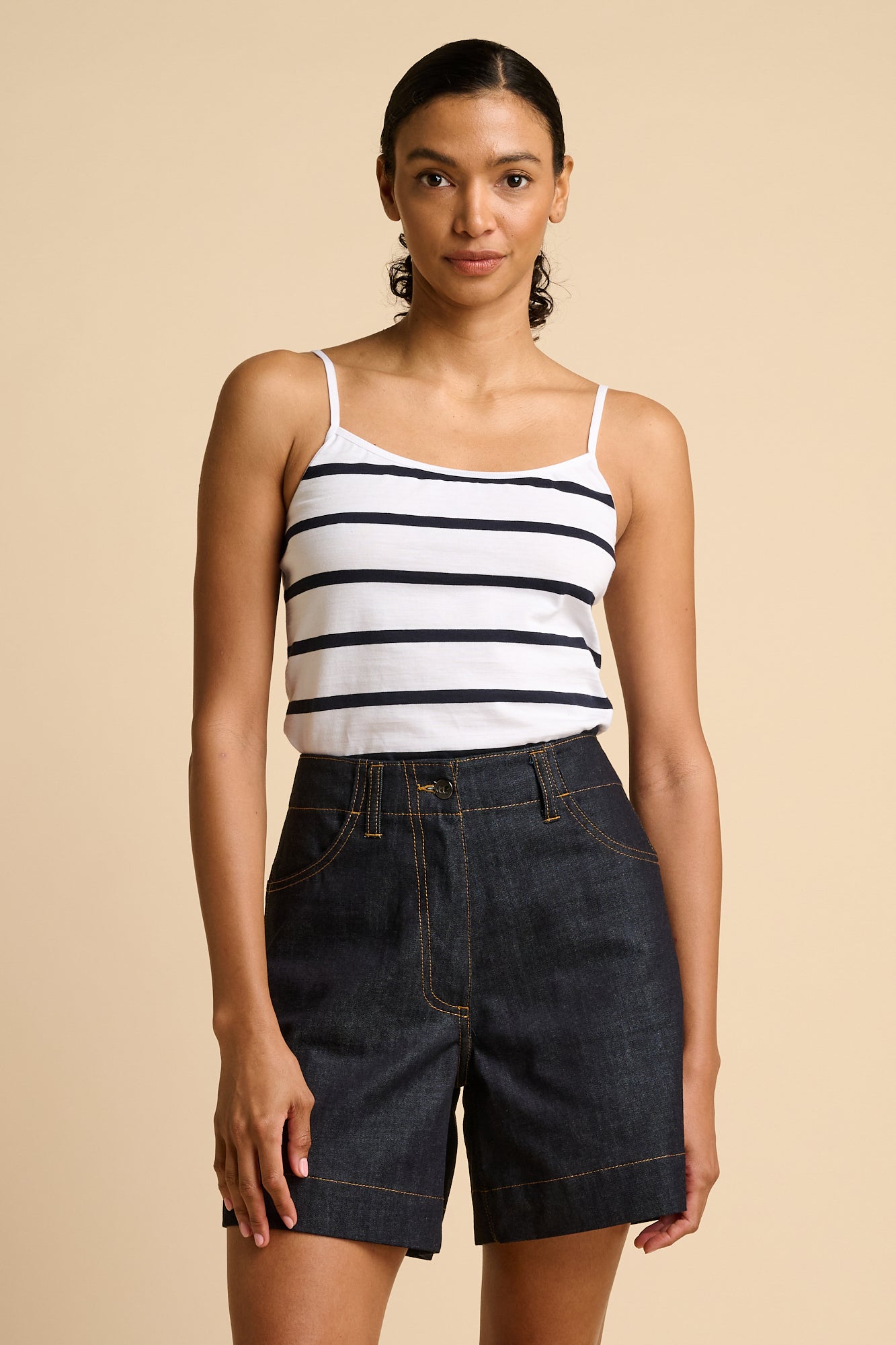 Woman wearing a striped tank top and denim shorts on a beige background