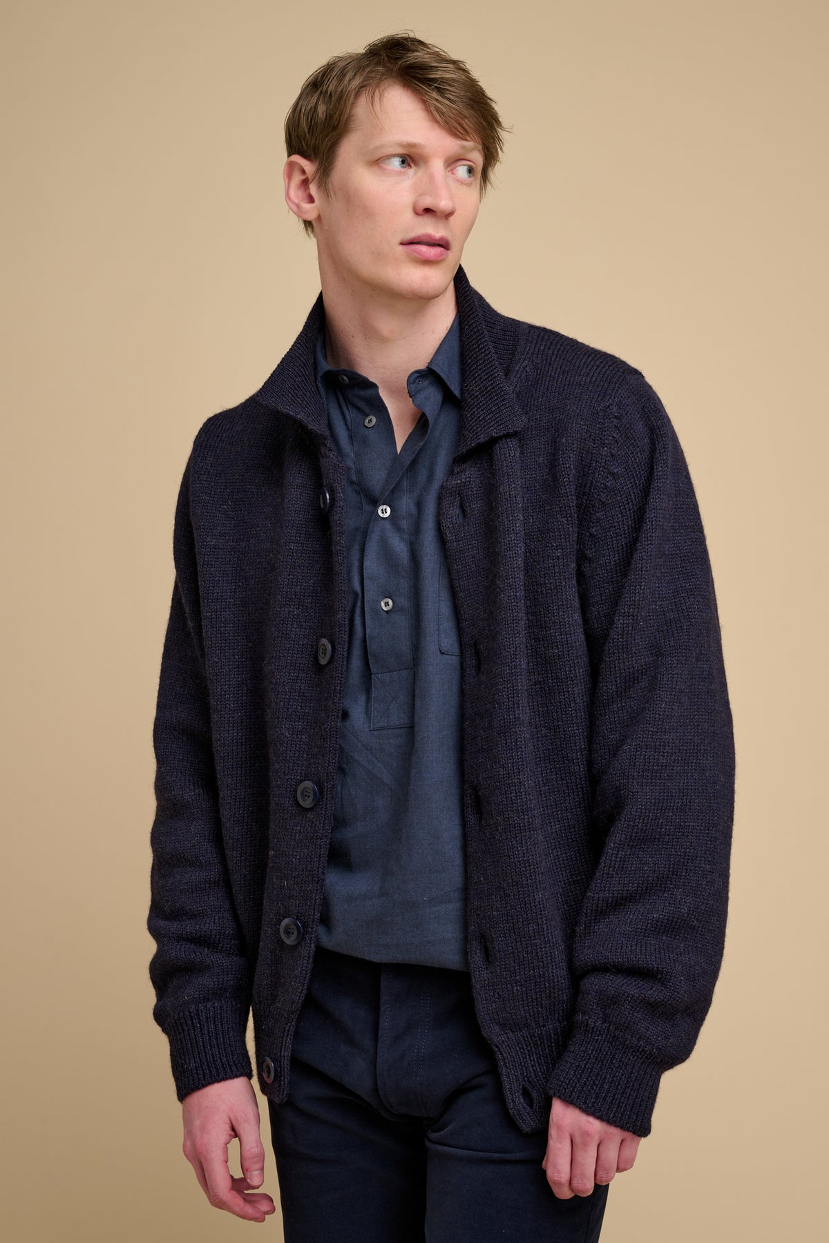 Man wearing a navy cardigan over a shirt on a beige background