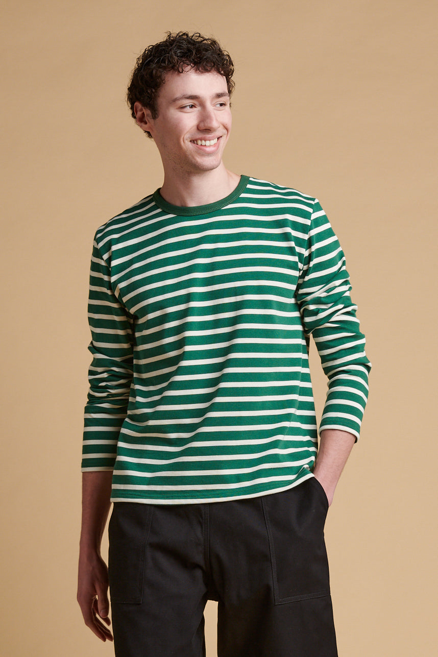 Thigh up front of smiley male wearing bottle green ecru stripe long sleeve Breton  top.