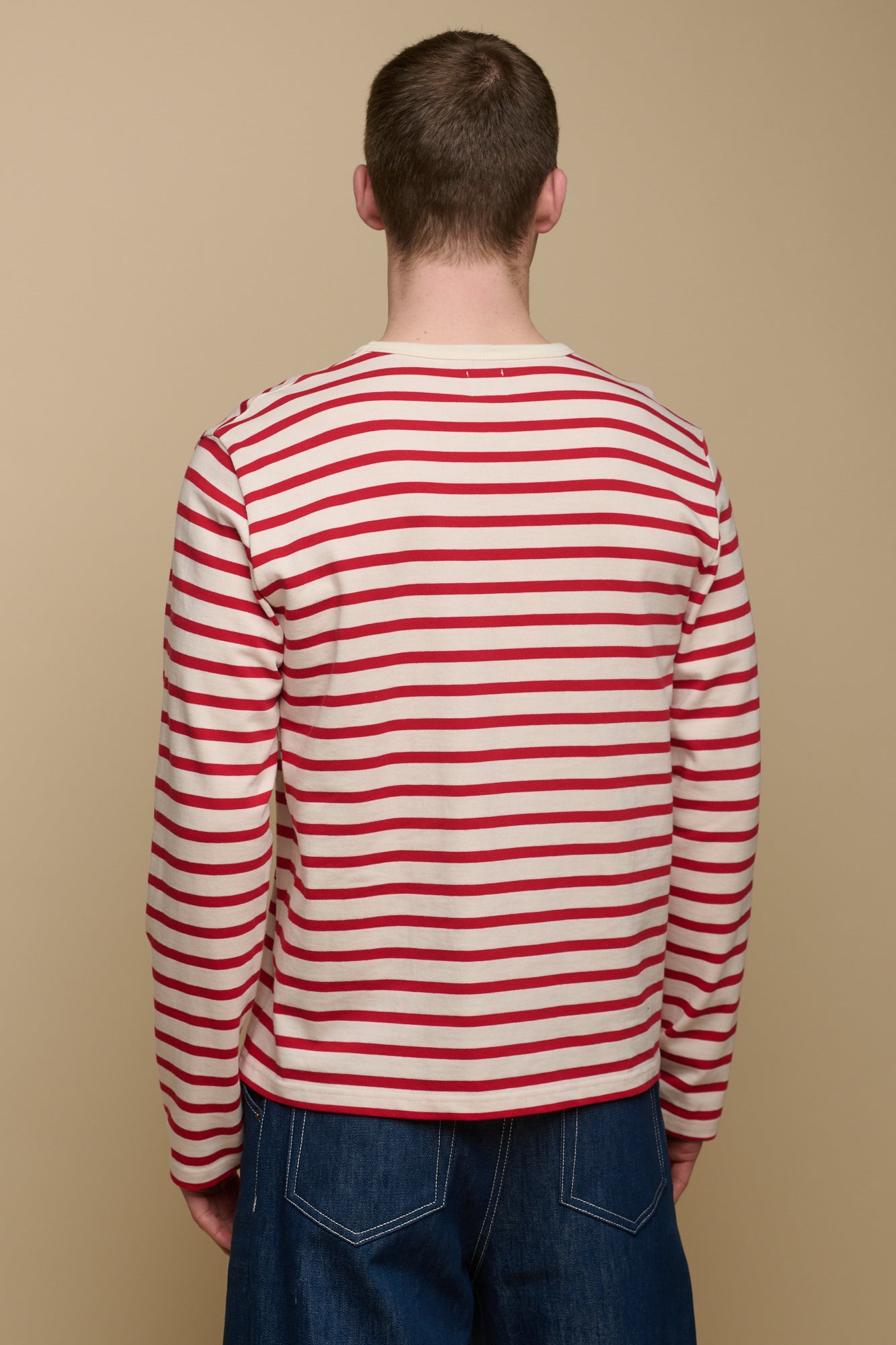 Thigh up of the back of brunet male wearing ecru/flame red Breton paired with men's jeans in blue