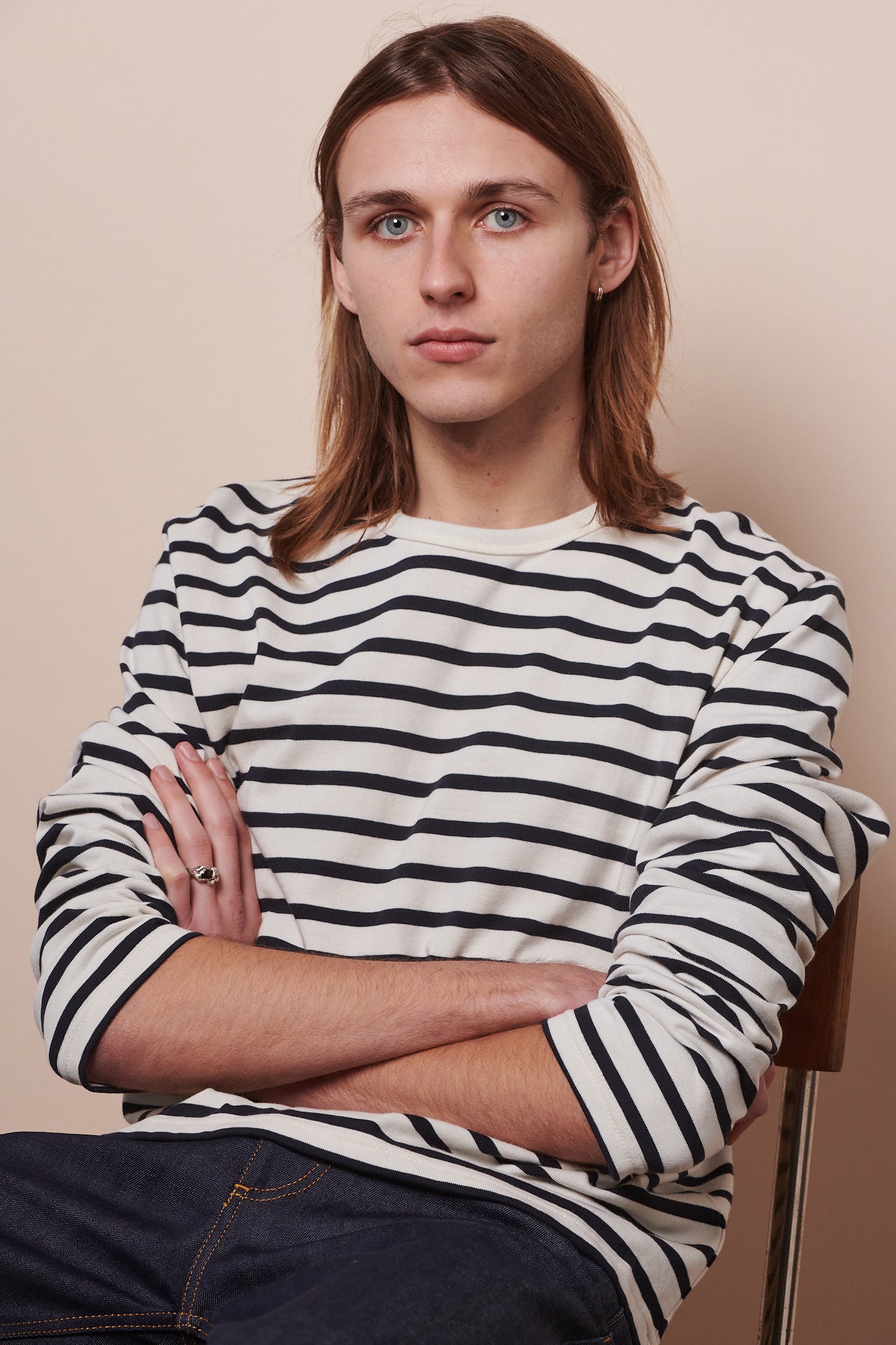 Image of male sat back into chair with arms folded and sleeves of breton ecru navy pushed up to elbows