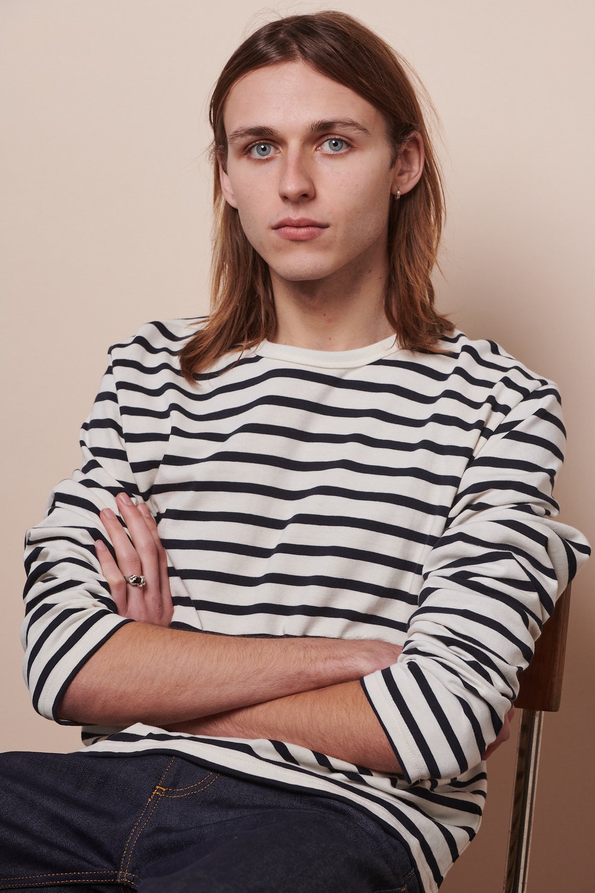 Image of male sat back into chair with arms folded and sleeves of breton ecru navy pushed up to elbows