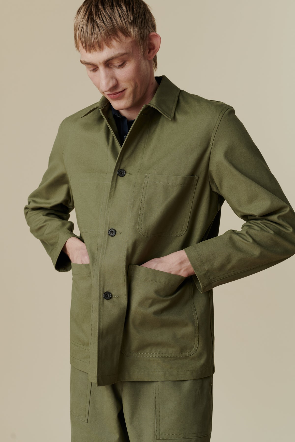 Image of white male wearing chore jacket in olive. Front pocket detail 