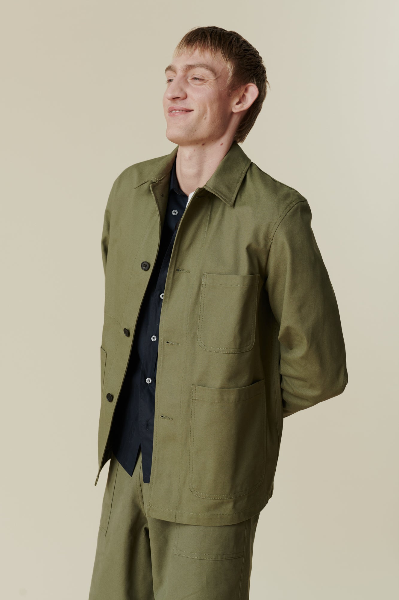 Image of white male, waist up wearing men's chore jacket in olive. Collar, button fastening detail, front pockets 