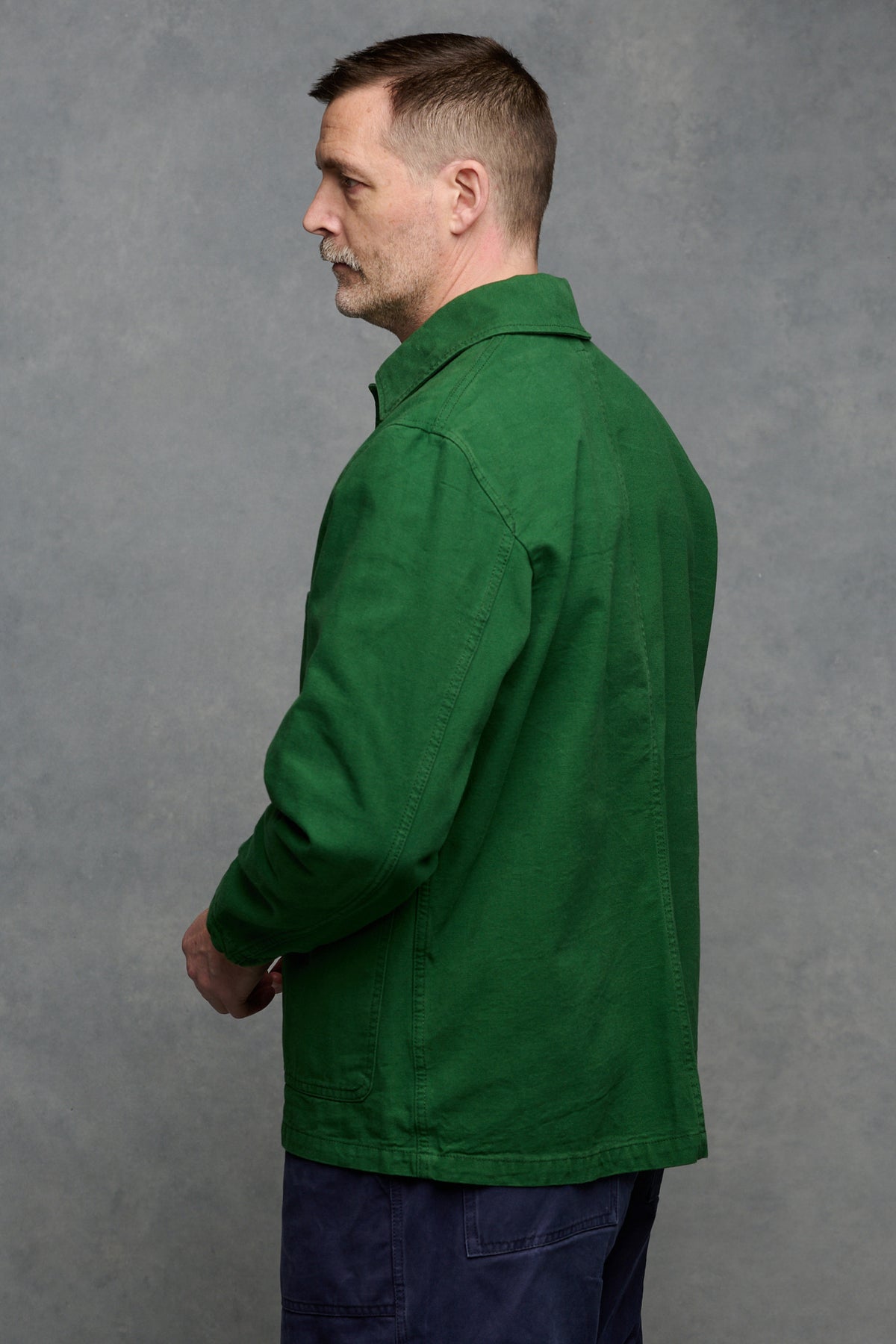 Thigh up image of the back of Patrick Grant wearing men's chore jacket in bottle green