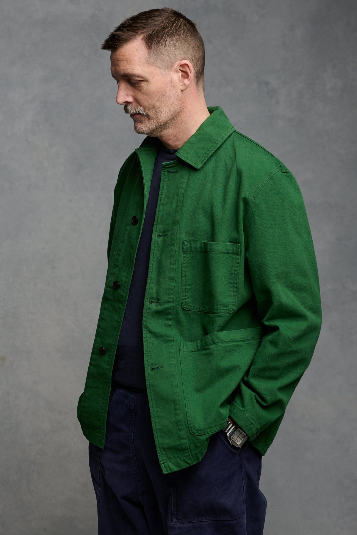 Thigh up image of Community Clothing founder Patrick Grant wearing men's chore jacket in bottle green, worn with cameraman pants in navy 