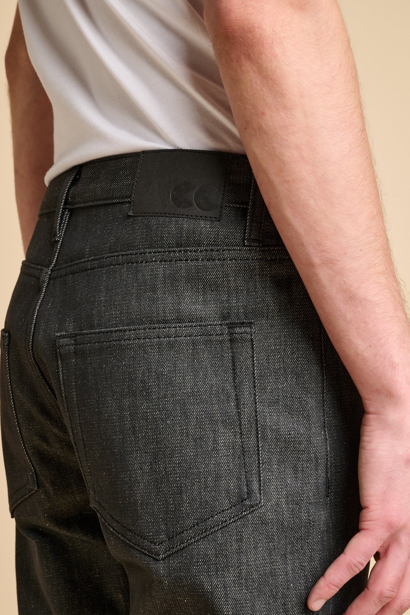 Close up of the back of man wearing black denim Darren jeans with black CC logo jeans patch.