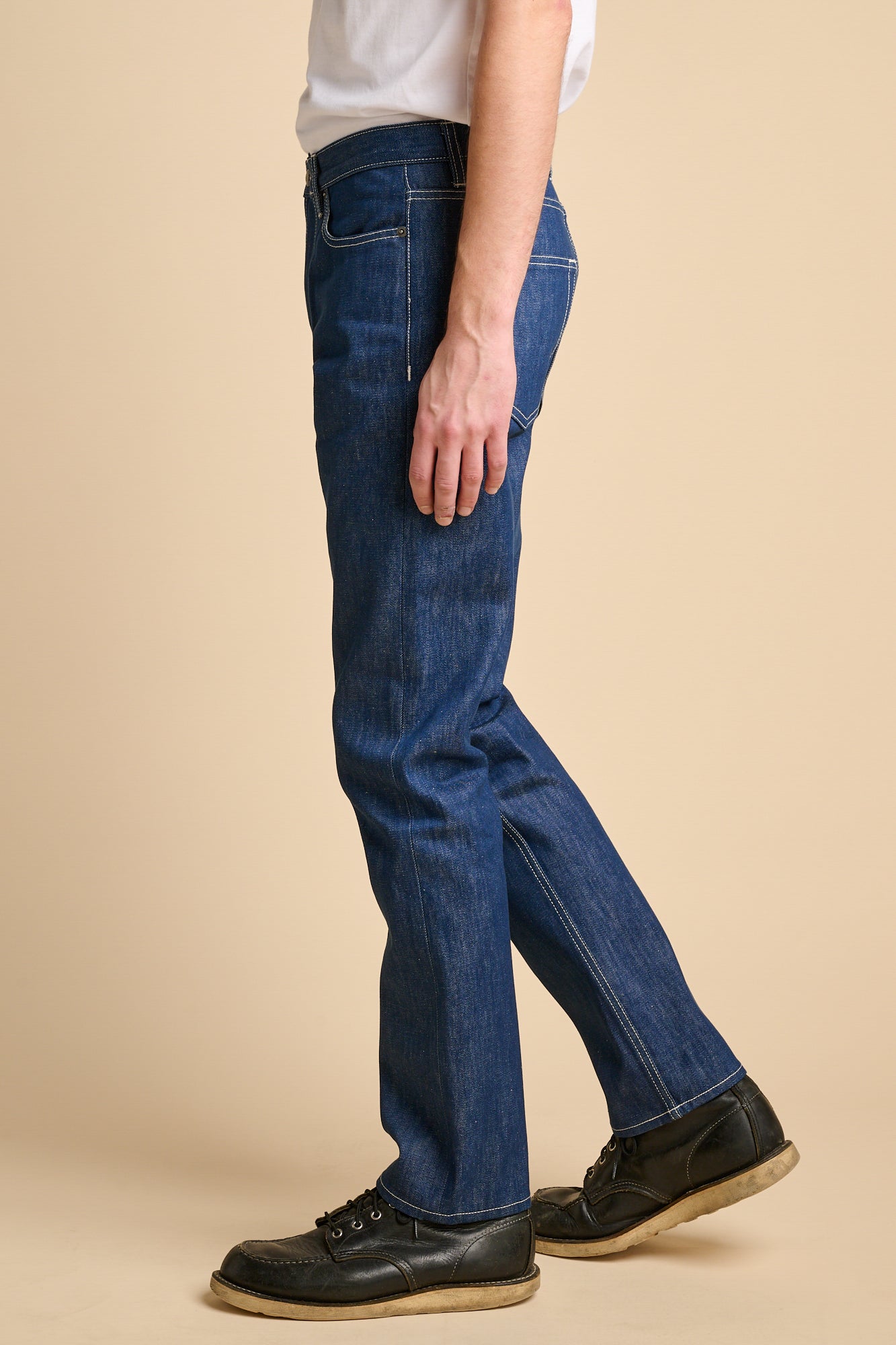 Man wearing straight cut jeans in blue with contrast ecru stitching.