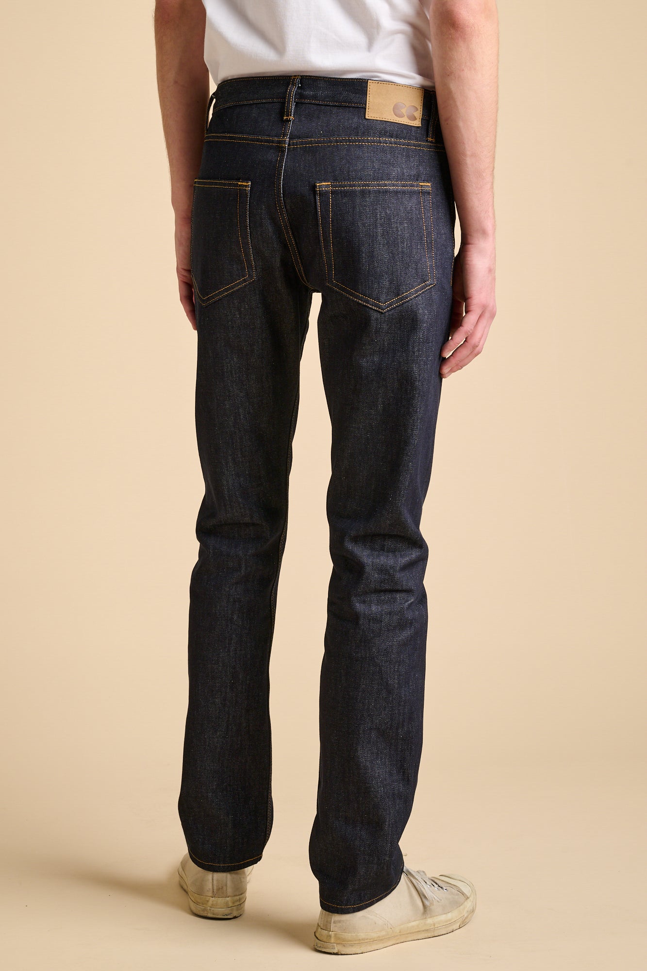 The back of man wearing straight cut jeans in indigo with contrast tobacco stitching. 