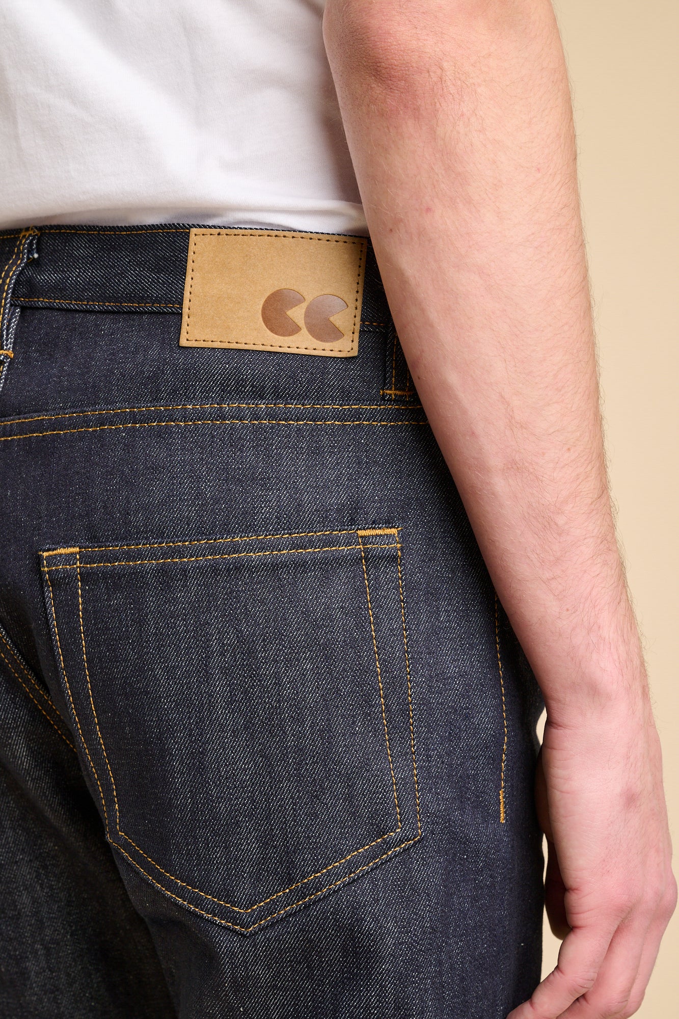 Close up of the back of man wearing straight cut jeans in indigo with contrast tobacco stitching and CC logo jeans patch.
