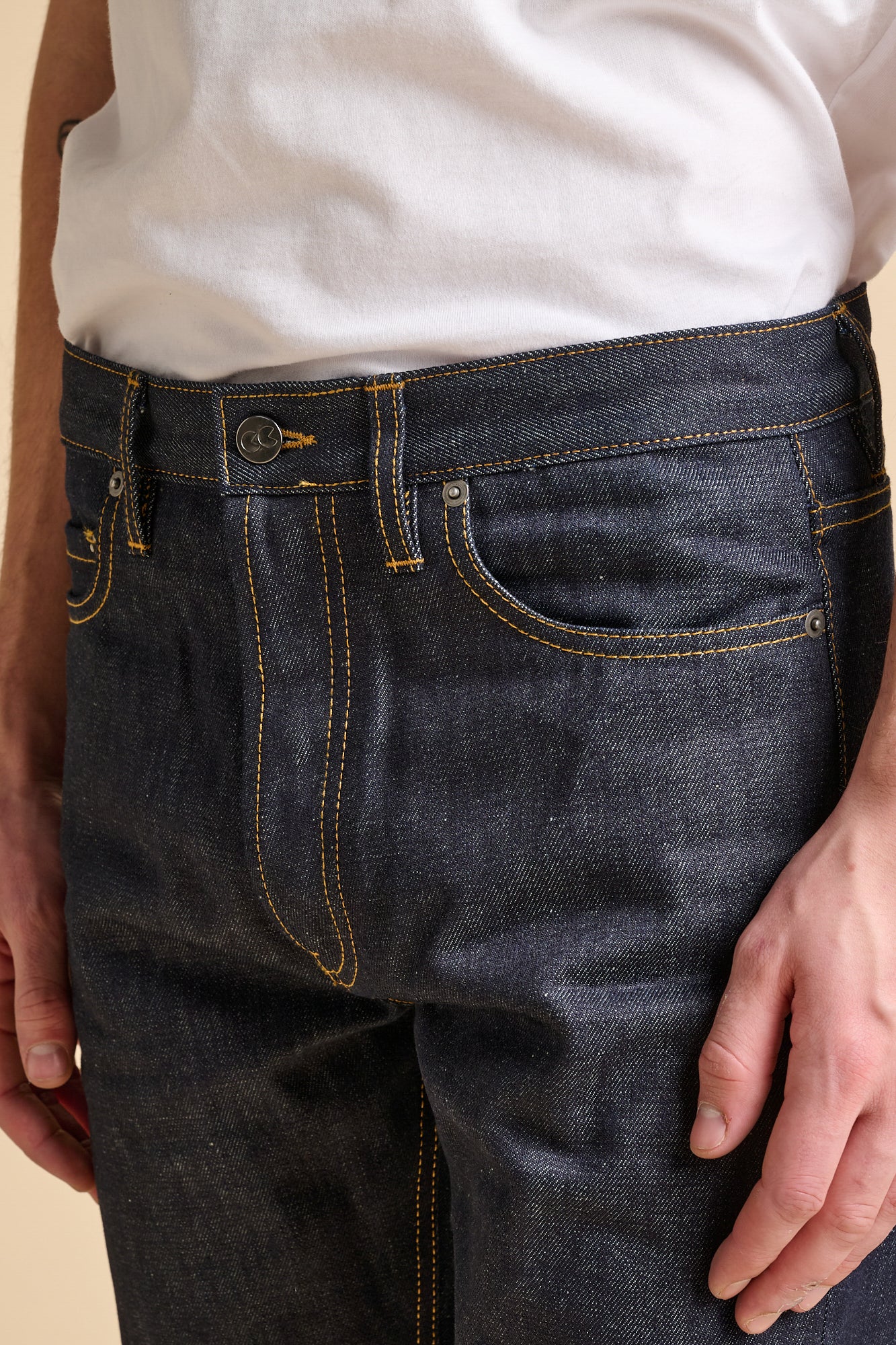 Close up of man wearing straight cut jeans in indigo with contrast tobacco stitching and CC logo button fastening,