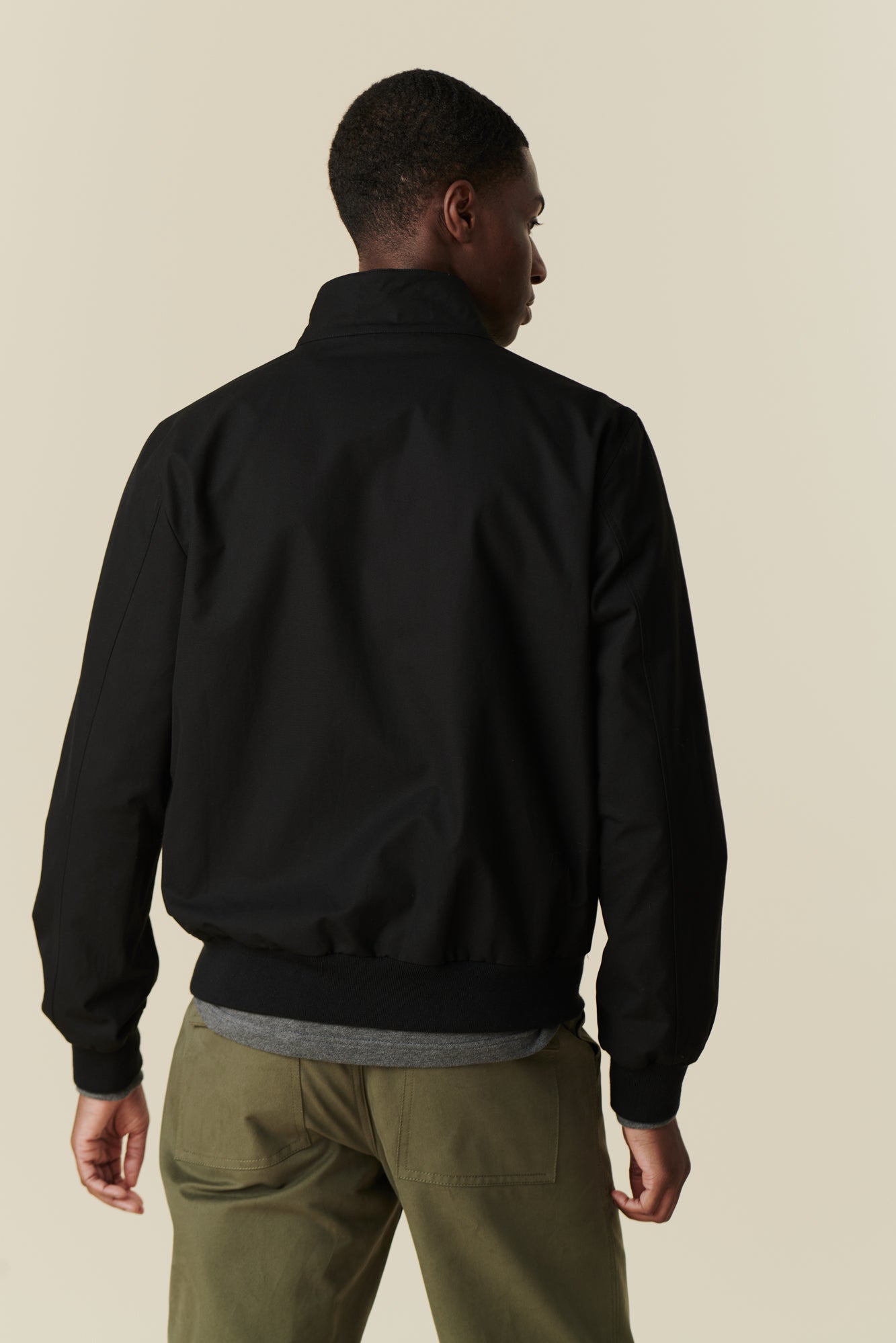 Back of black male wearing black Harrington jacket paired with olive combat trousers.