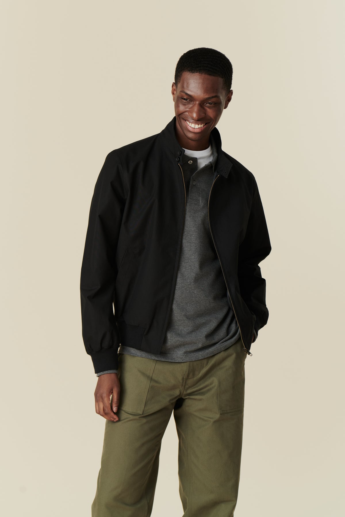 Front of smiley black male wearing black Harrington jacket over grey long sleeve polo