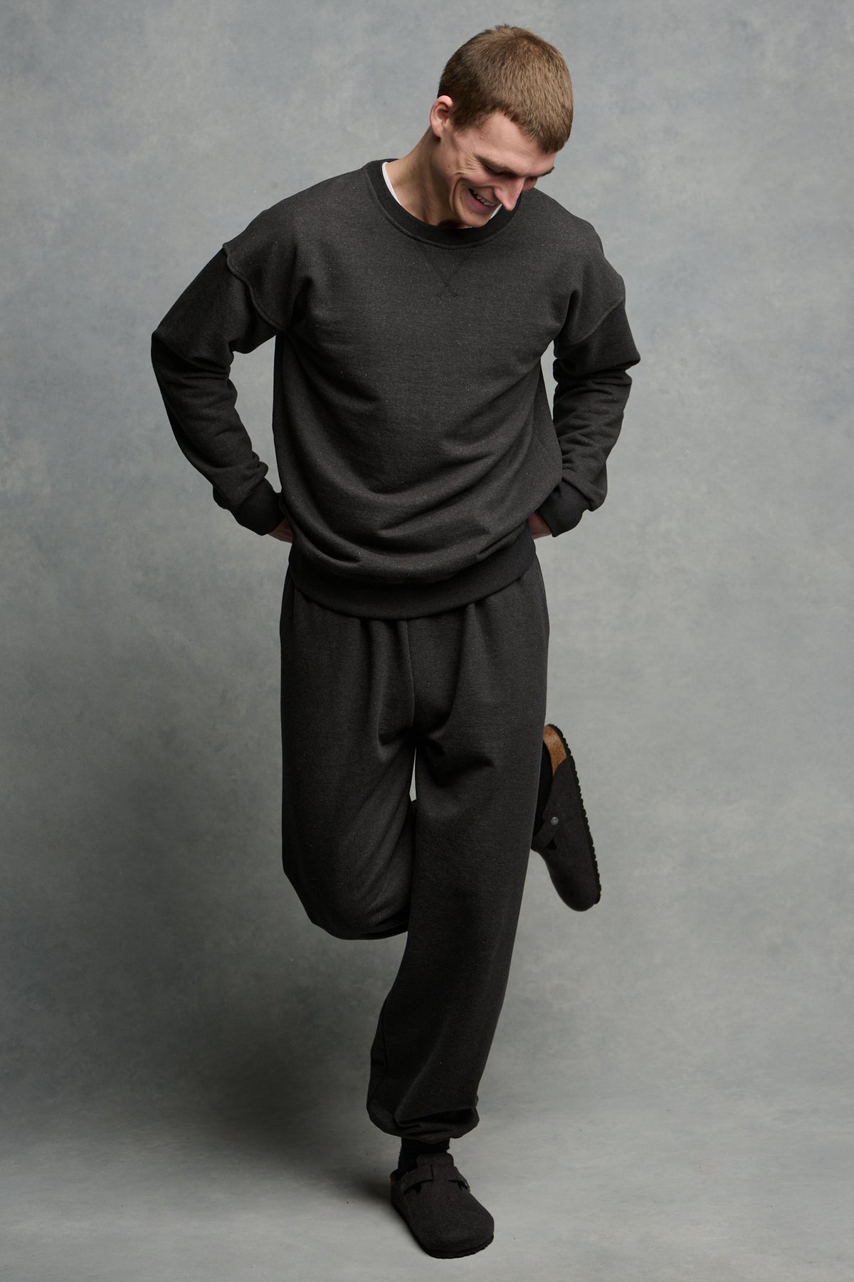 Full body image of male wearing heritage sweatshirt in charcoal looking down to the ground with matching sweatpants 