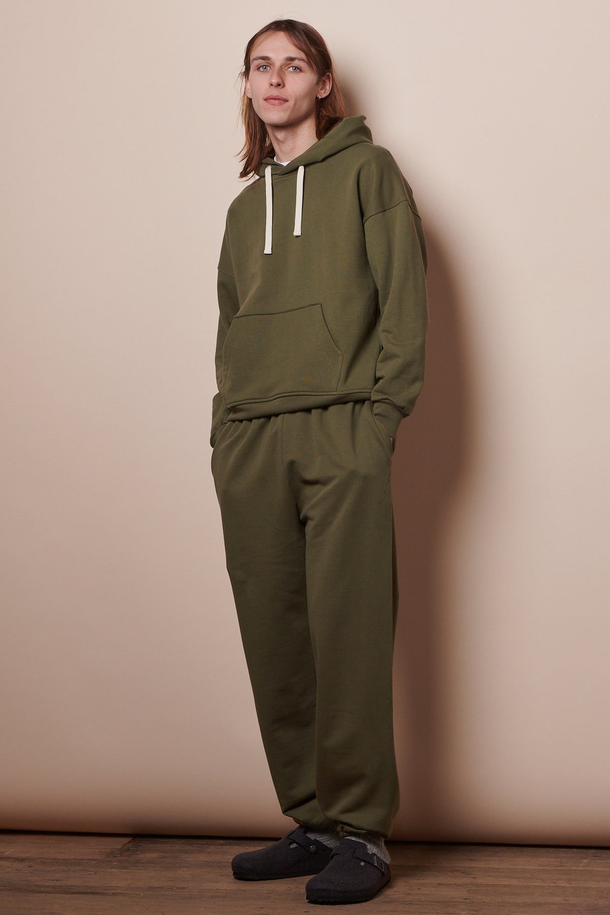 Full body image of male wearing hooded sweatshirt in olive paired with matching sweatpants 