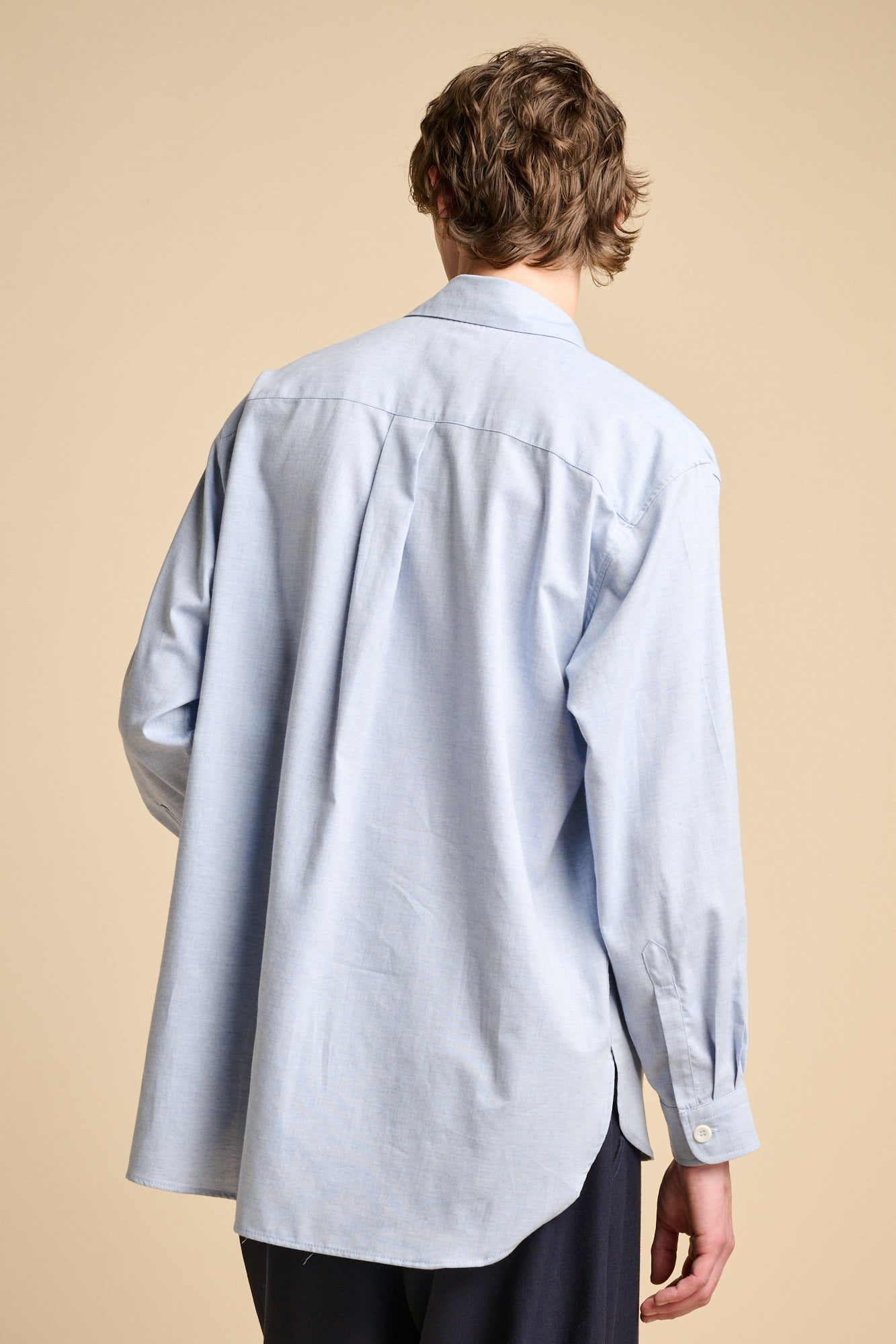 The back of a man wearing long sleeve, loose fit, light blue shirt.