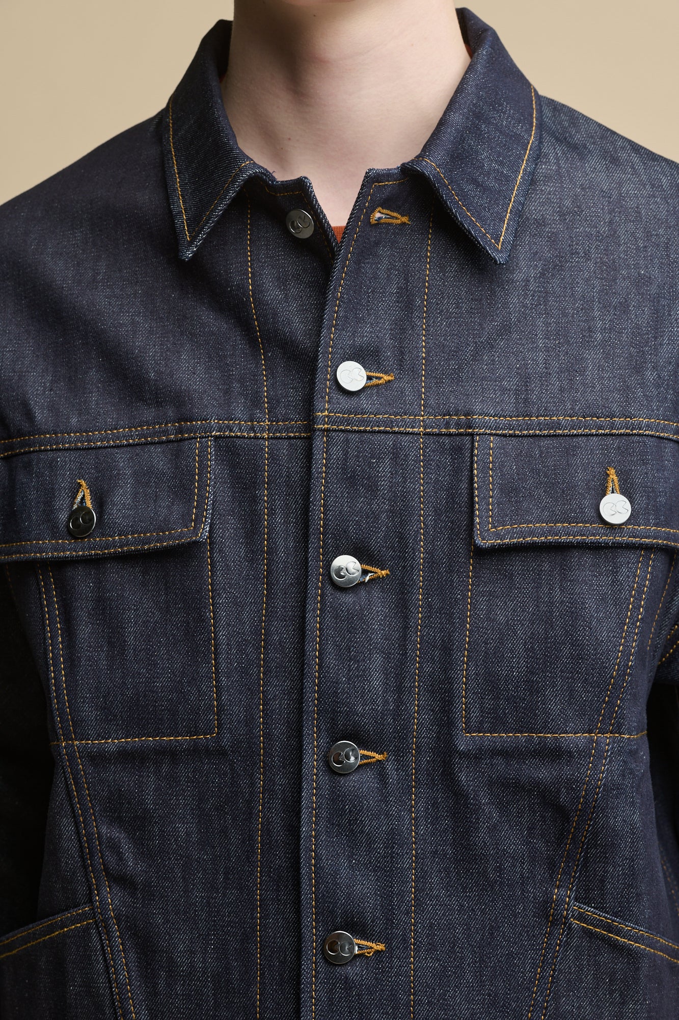 Detail shot of the front of Joe Denim Jacket in indigo, two front chest pockets with flap and button fastenings, CC logo branded buttons