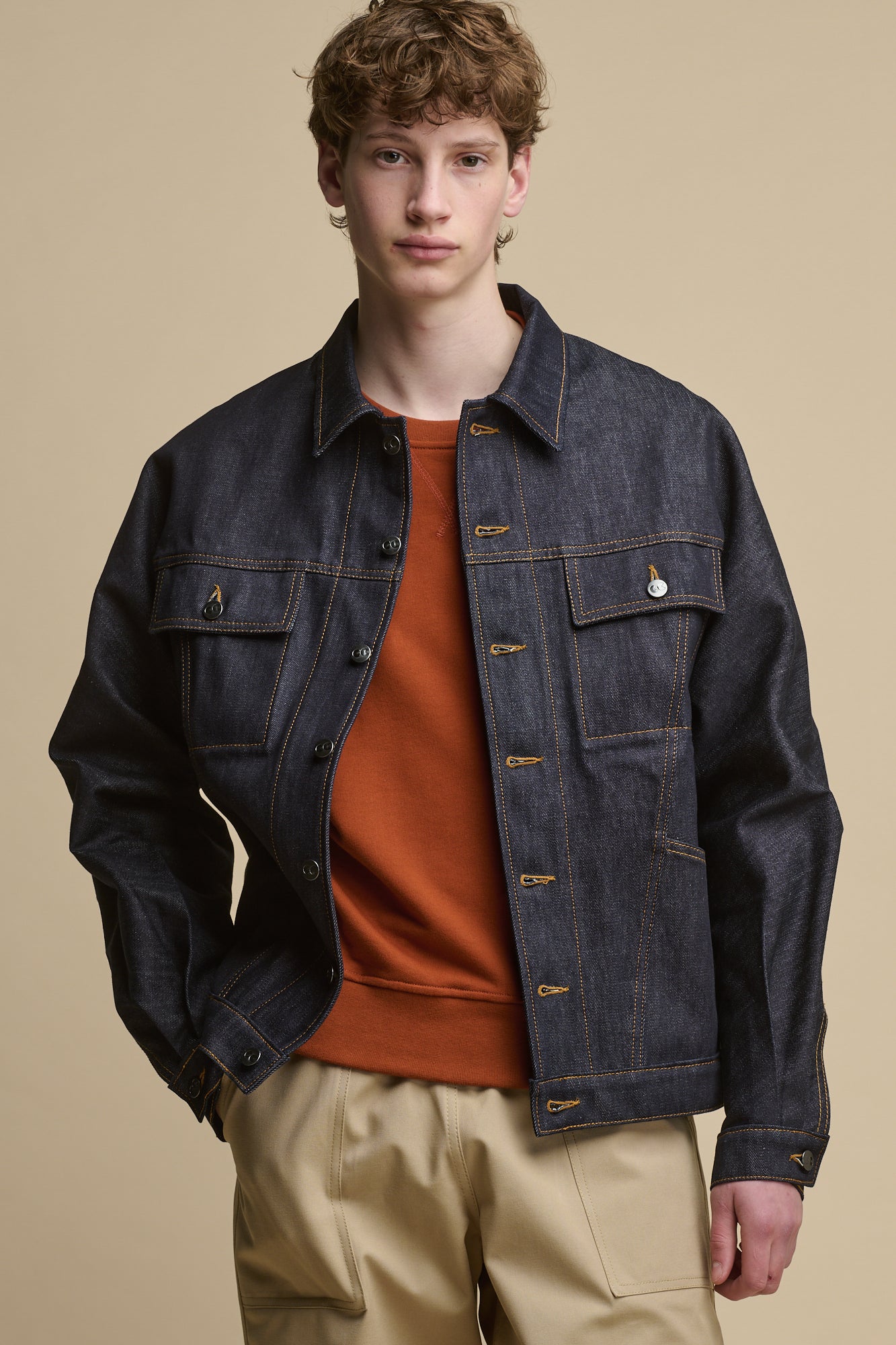 Thigh up image of the front of male wearing joe denim jacket in indigo worn over cinnamon raglan sweatshirt