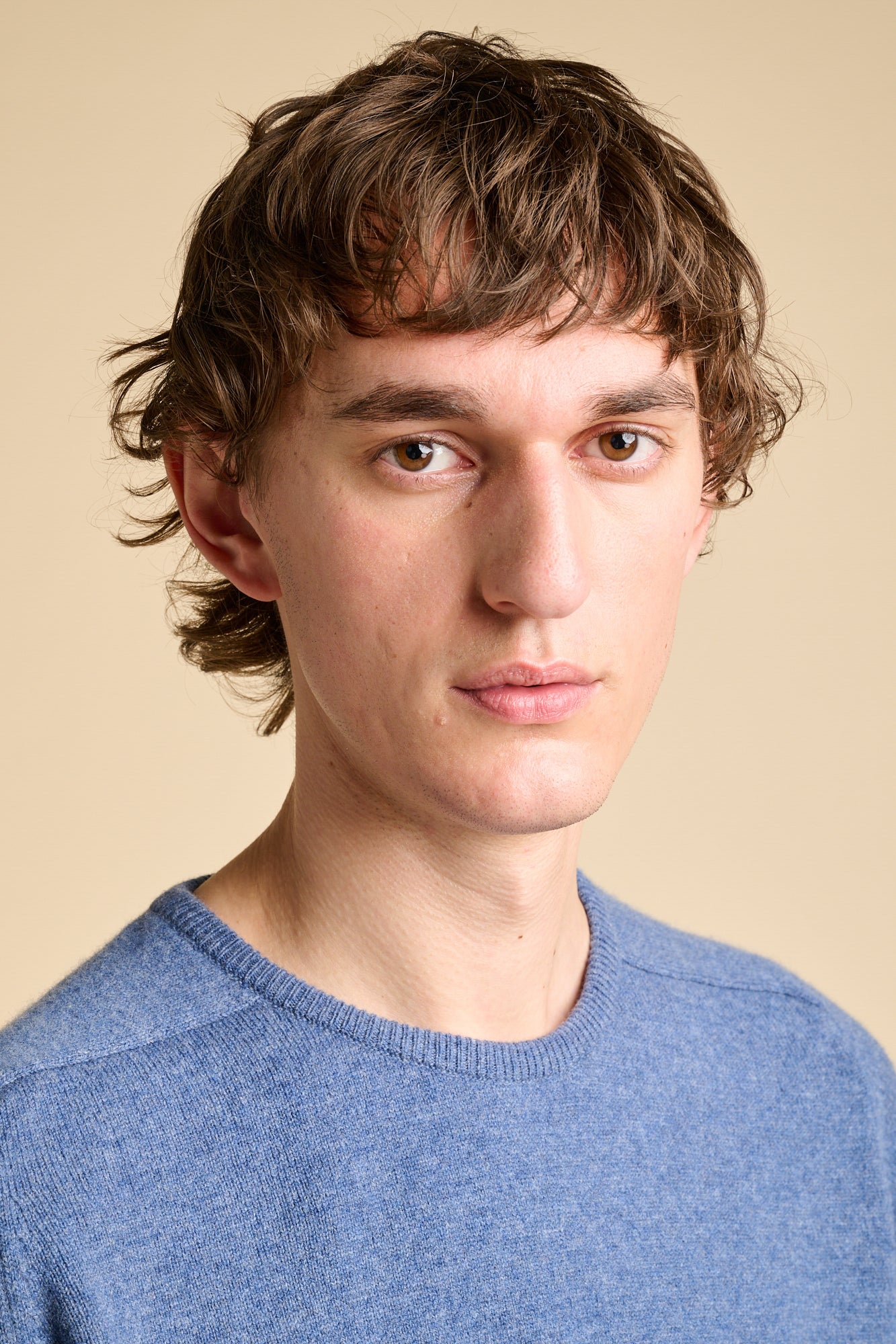 Portrait of man wearing lambswool saddle shoulder crew neck jumper in denim blue.