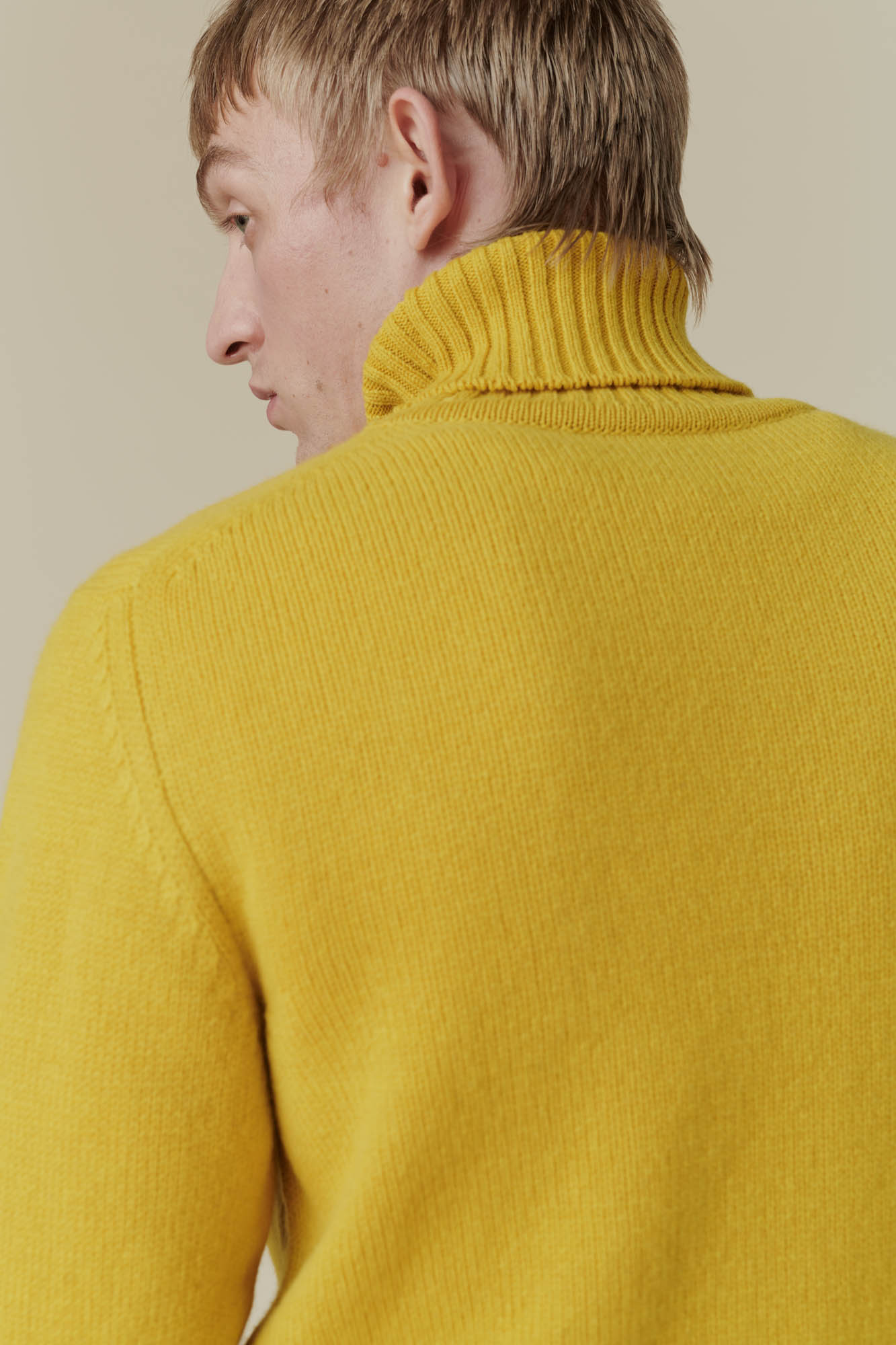 Waist up shot of blonde male wearing mustard lambswool roll neck 