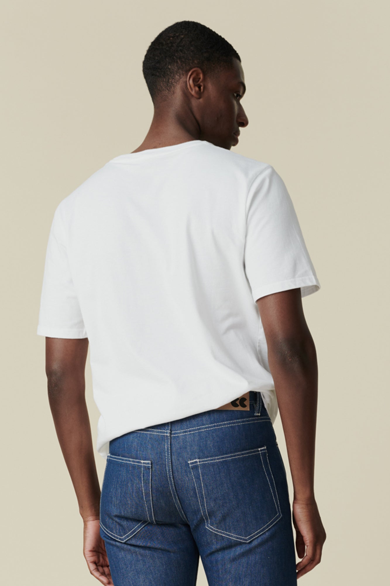 Thigh up image of smiley, black male with arms folded wearing white t shirt with community logo in black on chest