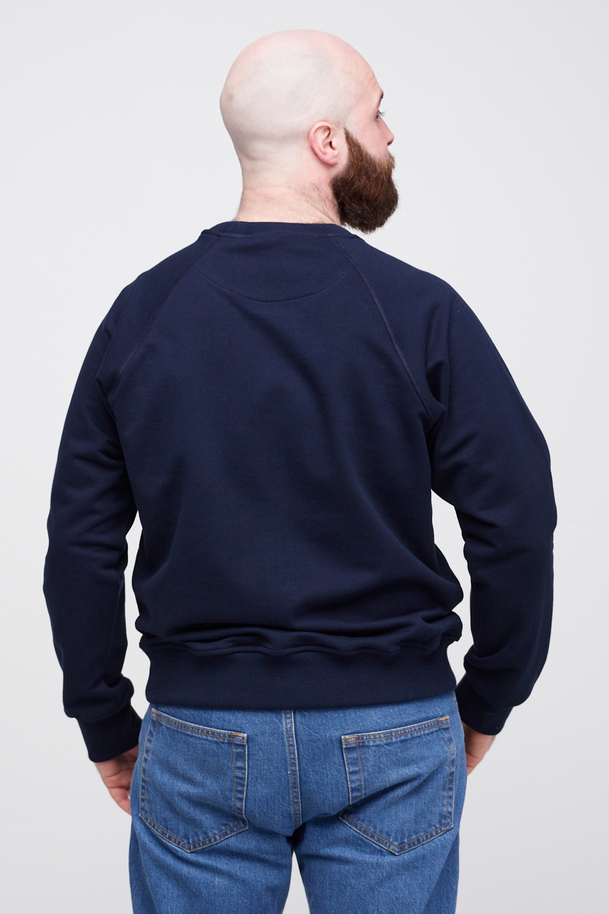 Man wearing a navy blue sweatshirt and blue jeans on a white background