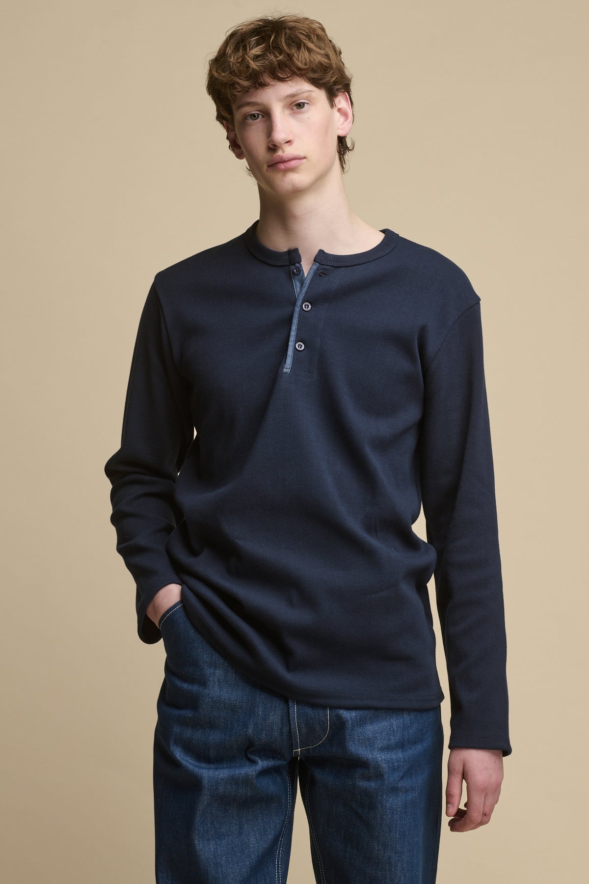 Thigh up image of male wearing Long Sleeve Henley top in Navy paired with men's blue jeans