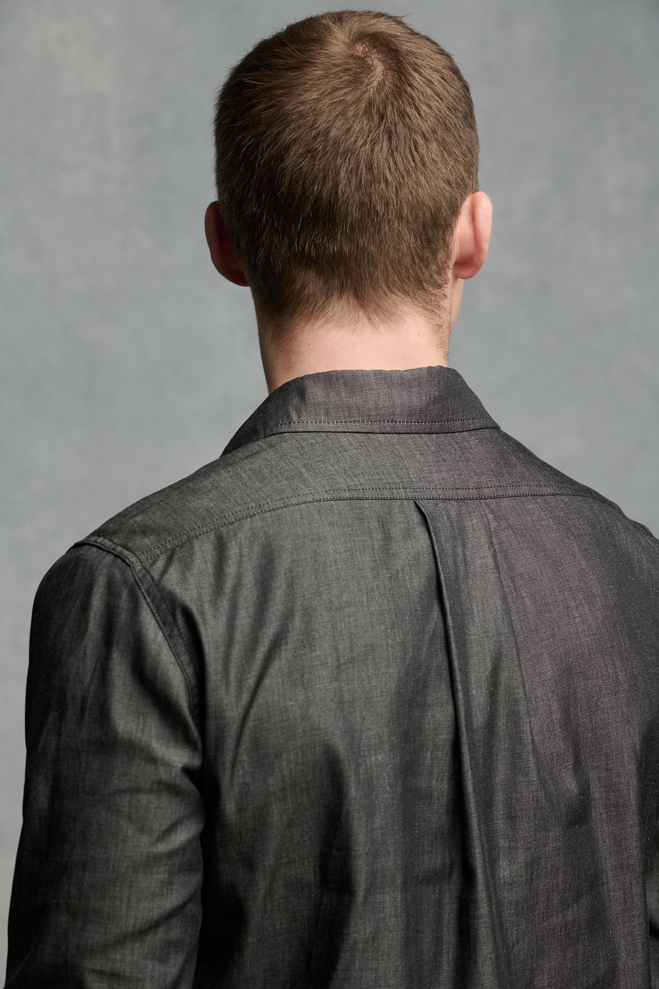 Thigh up front of male wearing Oli half placket lightweight denim shirt in black tucked into cameraman pants in black
