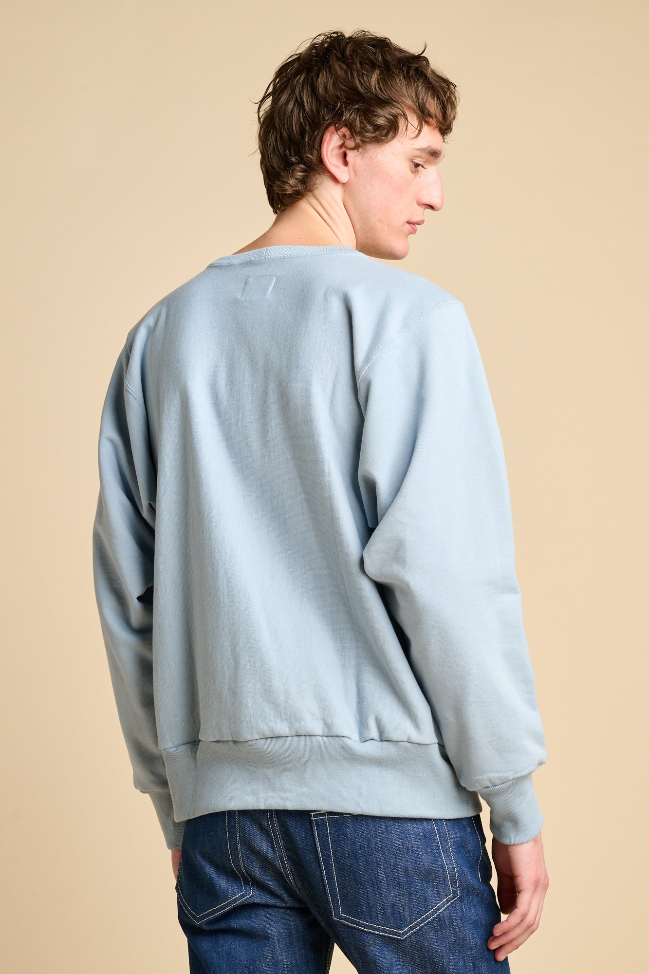 The back of man wearing sky blue oversized crew neck sweatshirt with jeans. 