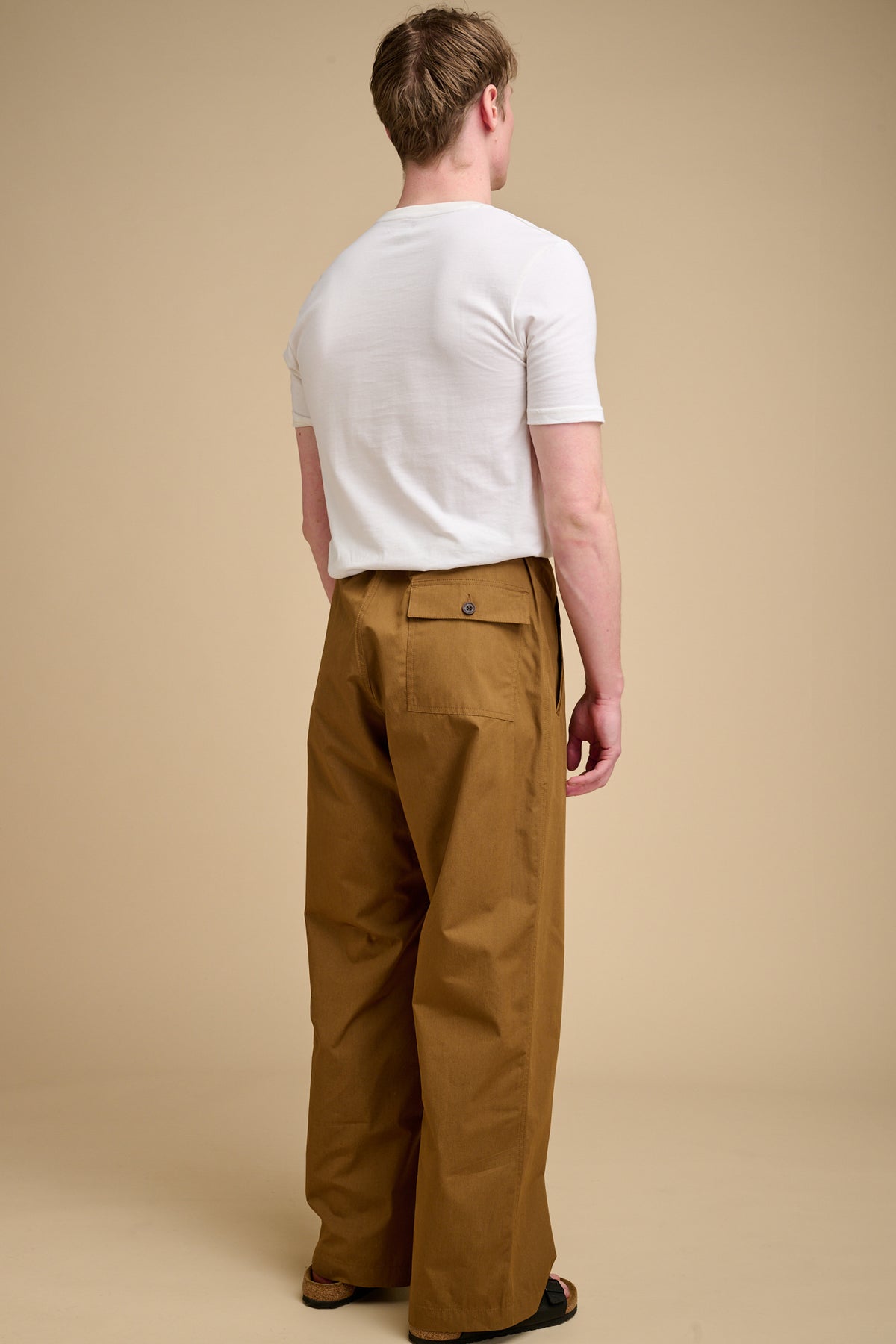 Man wearing a white t-shirt and tan pants against a beige background