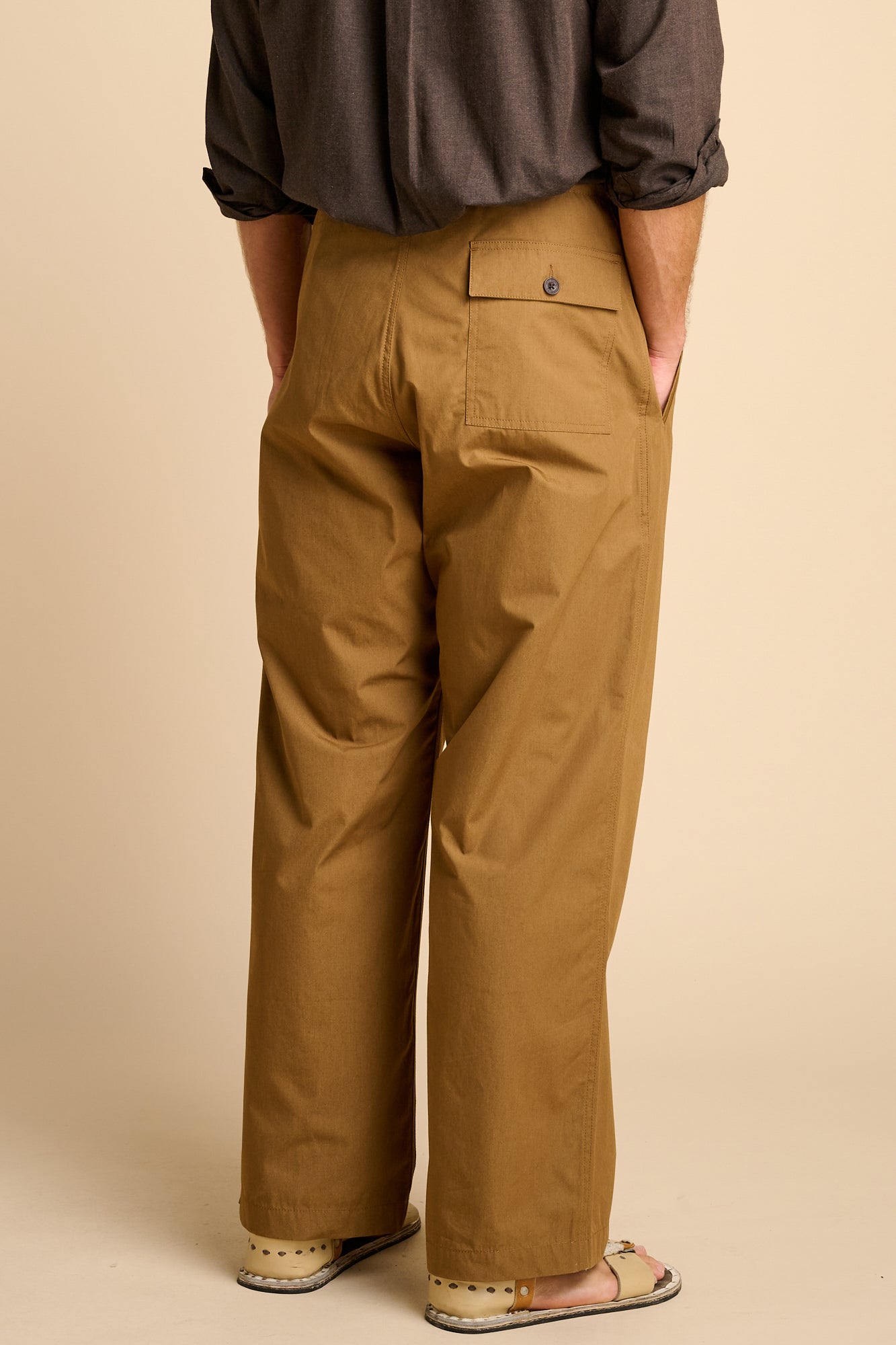 Man wearing tan trousers against beige background.