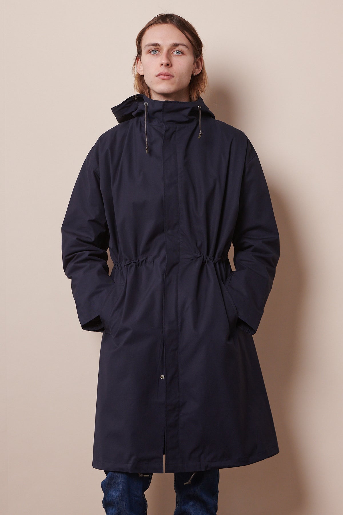Knee up image of the front of male wearing zipped parka in navy with hands in front pockets. 