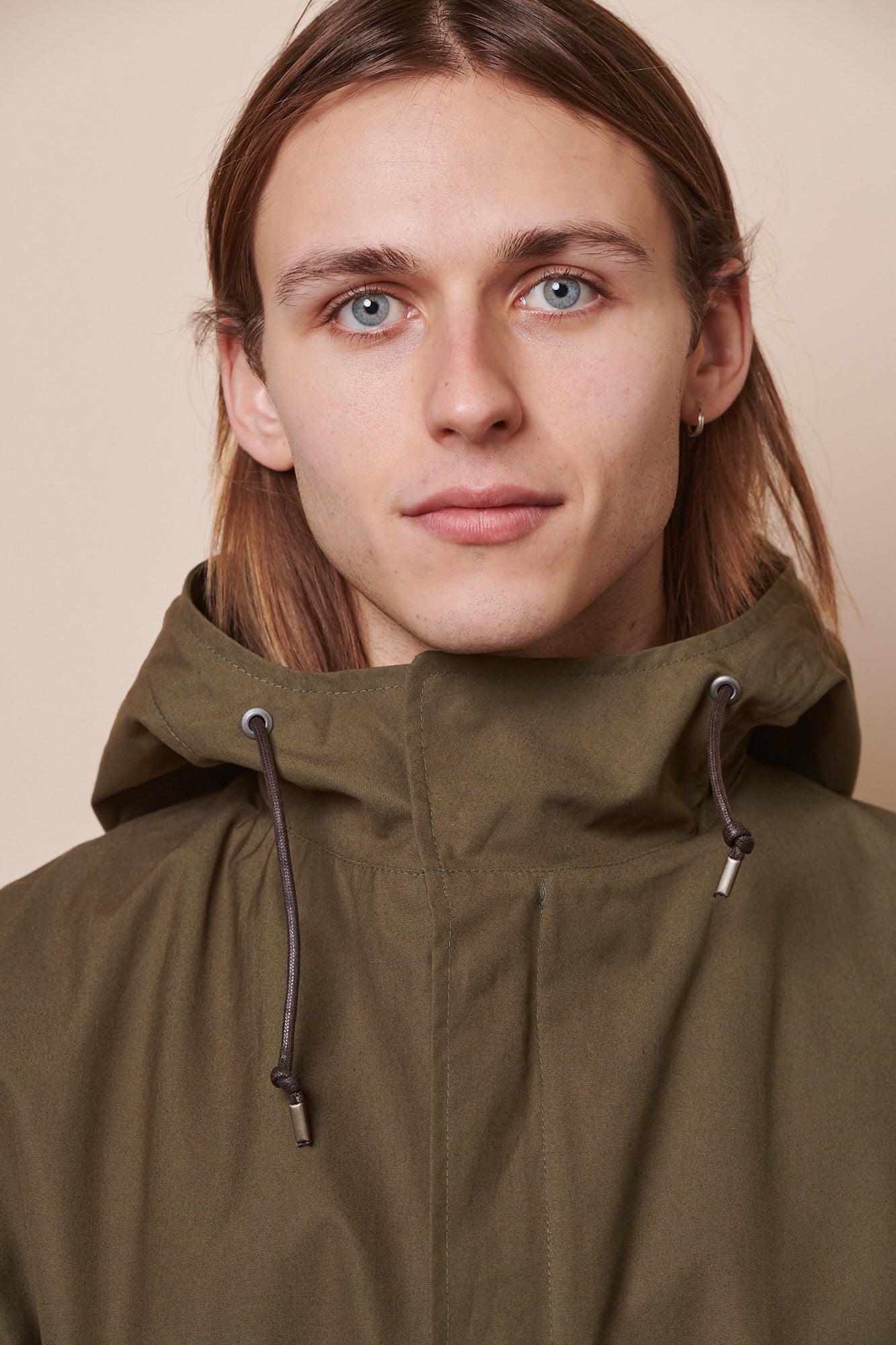 Portrait of male wearing zipped up parka in olive, showing drawcord through hood