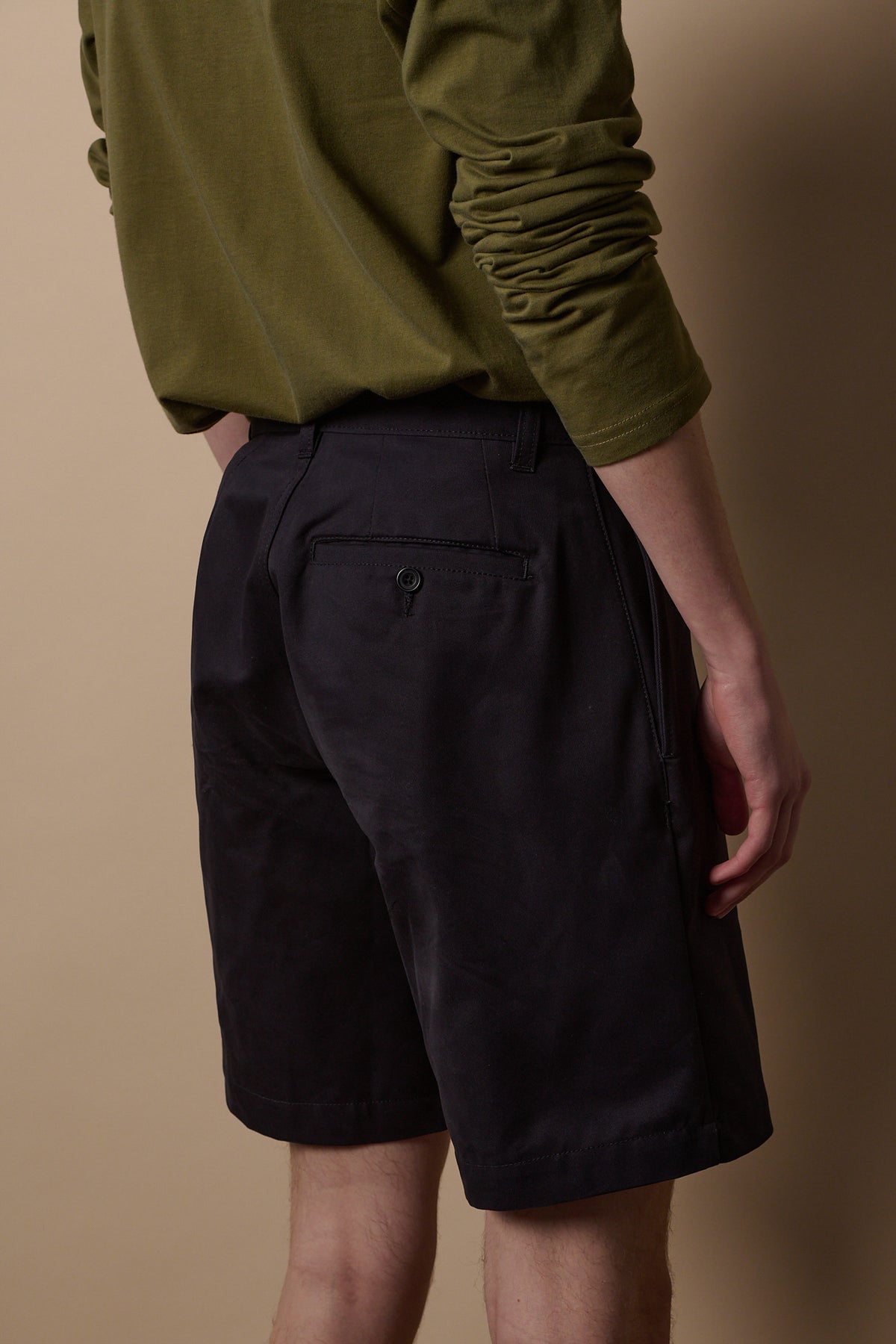 Back of pleated shorts in navy back pocket with button detail, beltloops on waistband