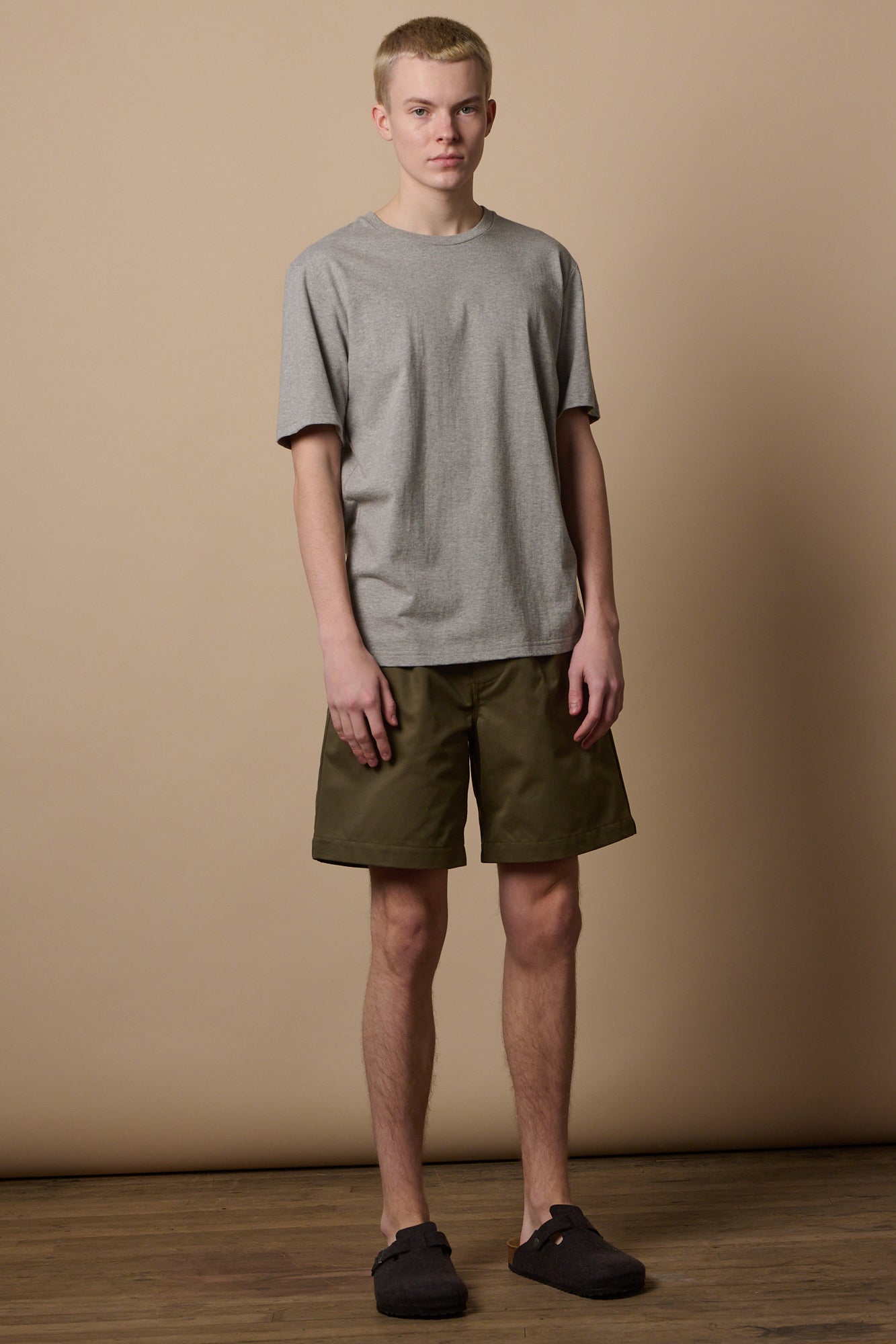 Full body image of male wearing pleated shorts in olive with short sleeve t shirt 