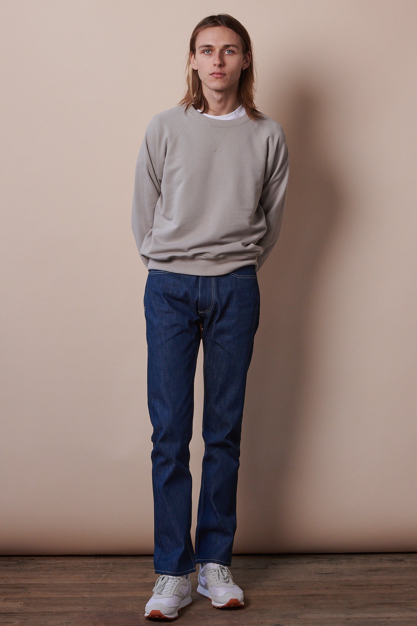 Full body image of male wearing raglan sweatshirt in stone paired with straight cut jeans in blue